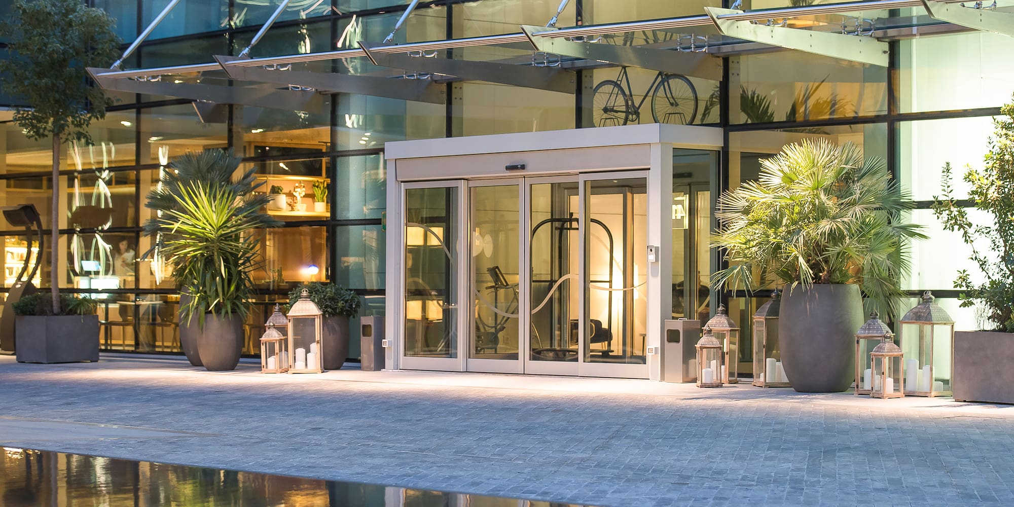 Contemporary hotel entrance: glass doors, potted palms, lanterns, reflecting pool.