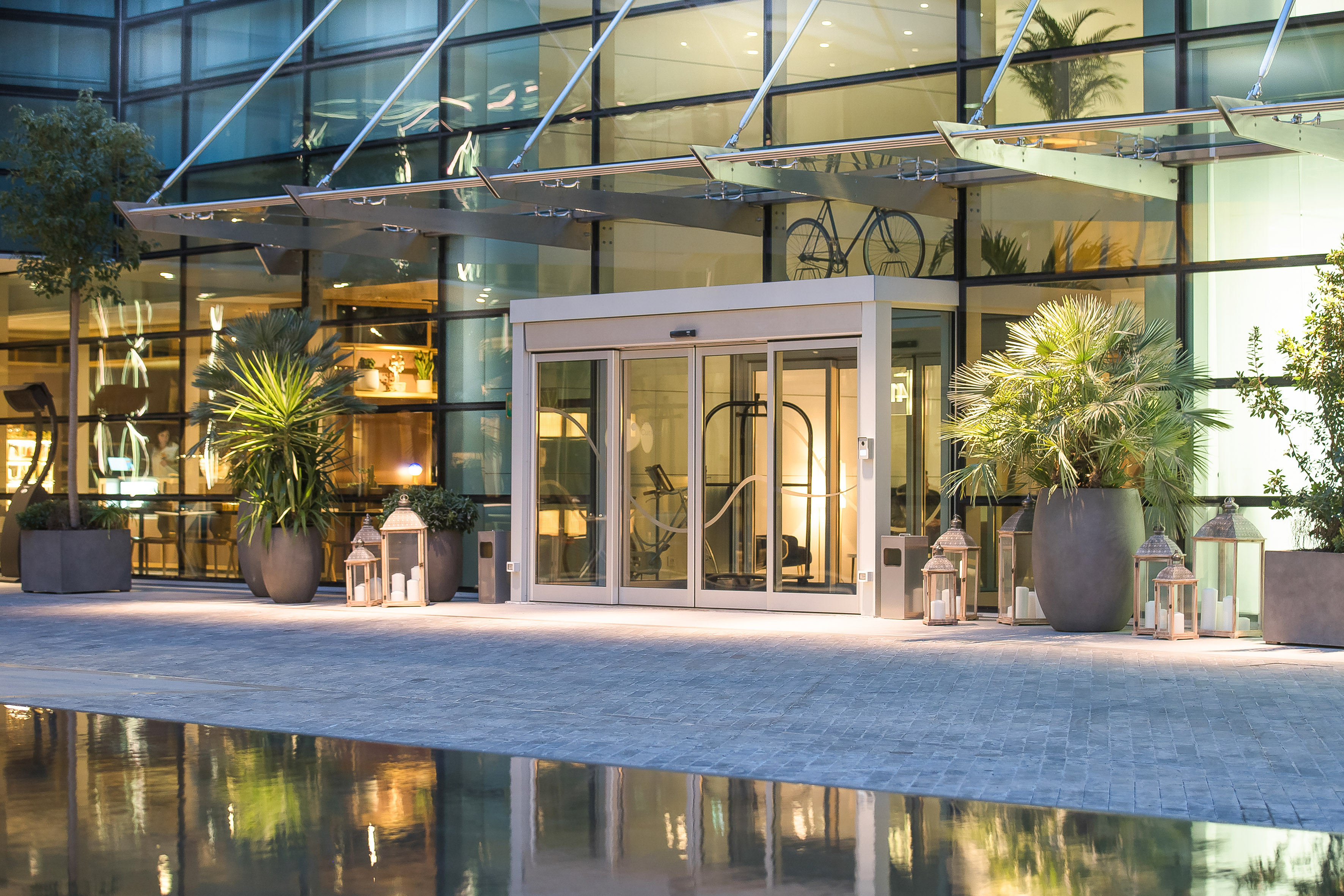 Contemporary hotel entrance: glass doors, potted palms, lanterns, reflecting pool.