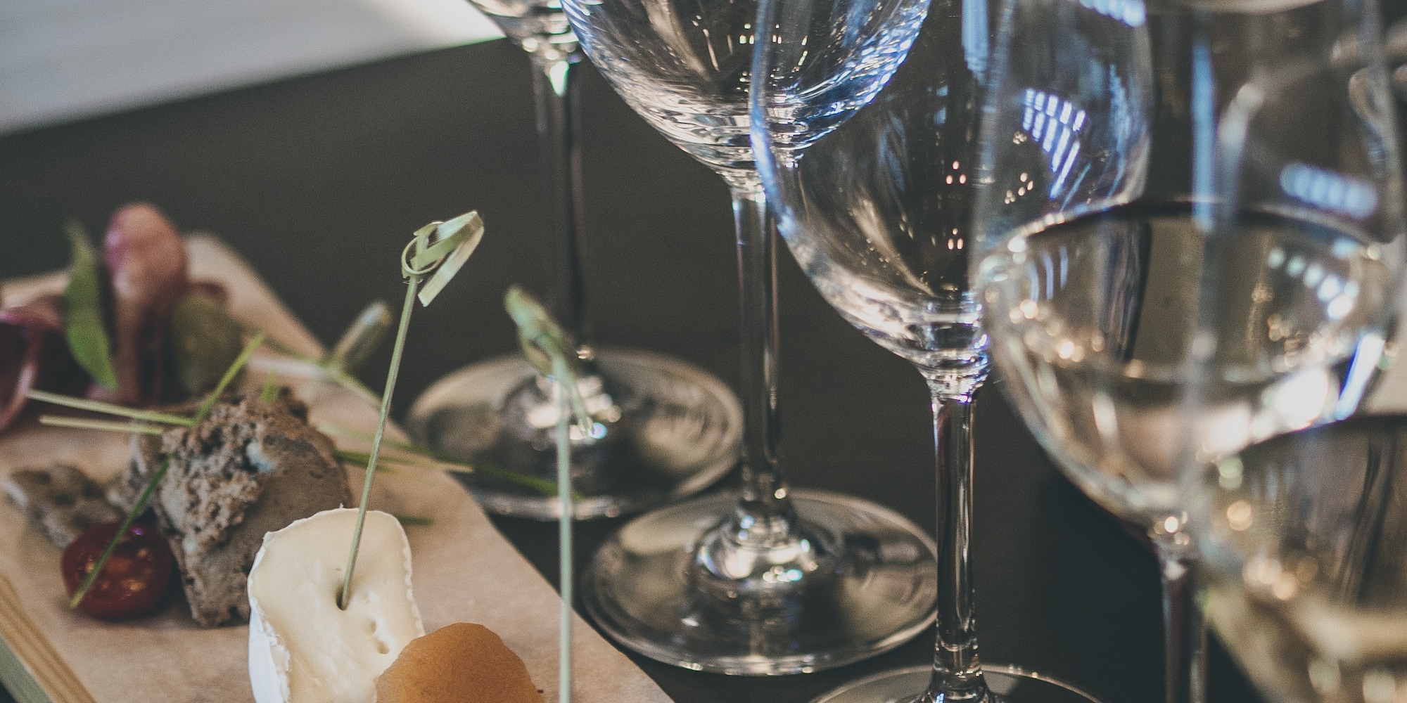 Empty wine glasses beside a tasting board with cheese, dried fruit, and pâté.