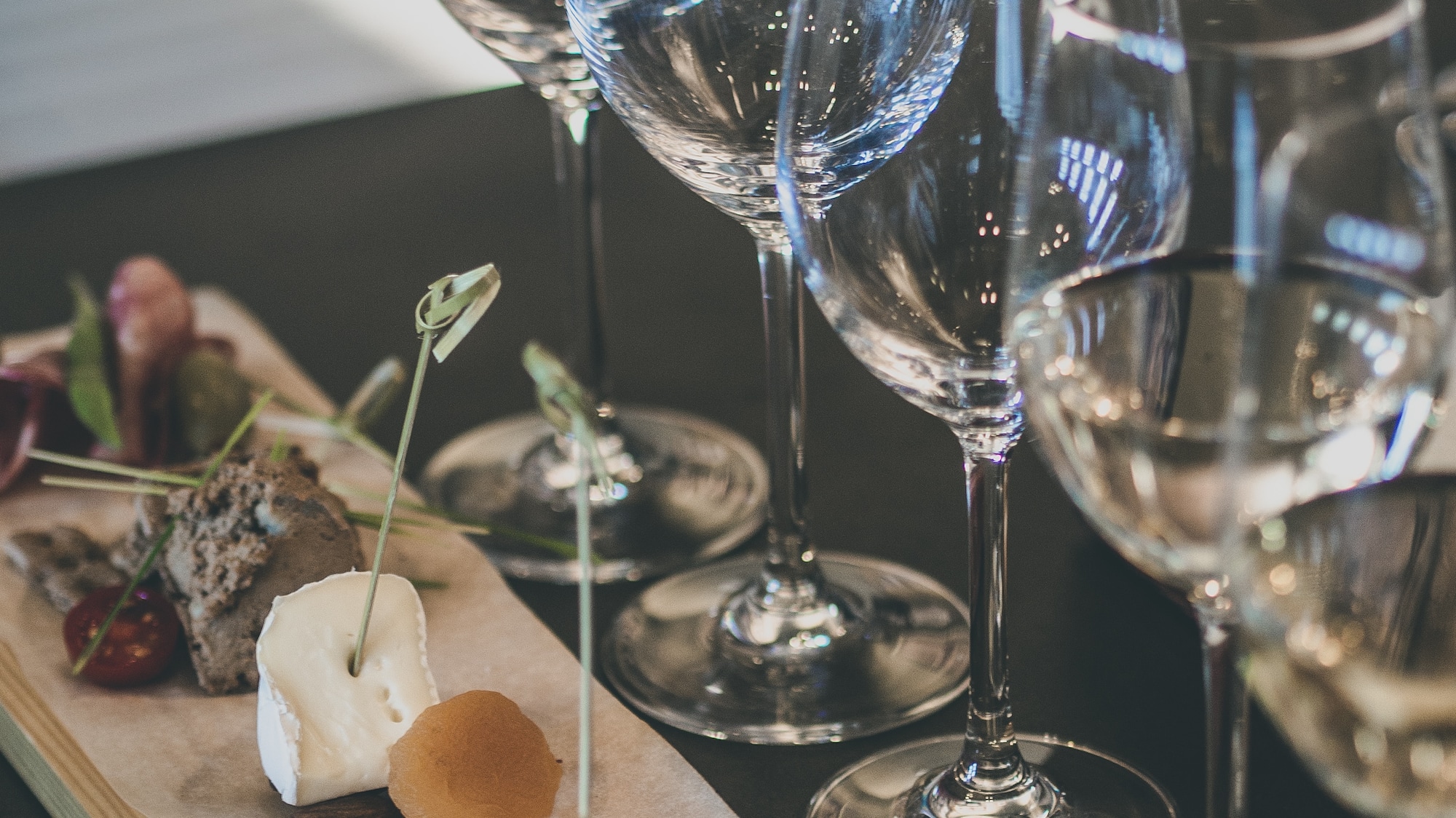 Empty wine glasses beside a tasting board with cheese, dried fruit, and pâté.