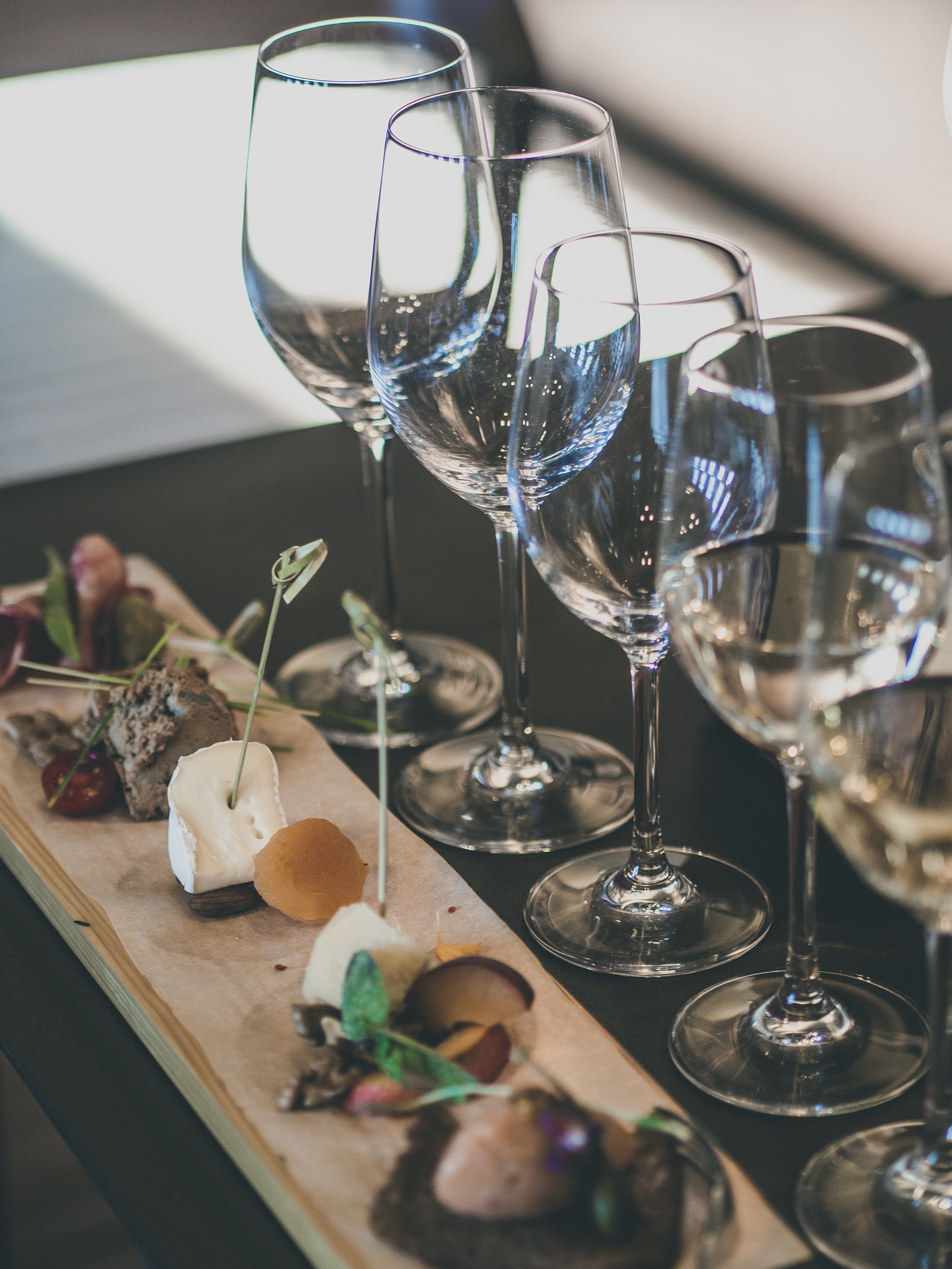 Empty wine glasses beside a tasting board with cheese, dried fruit, and pâté.