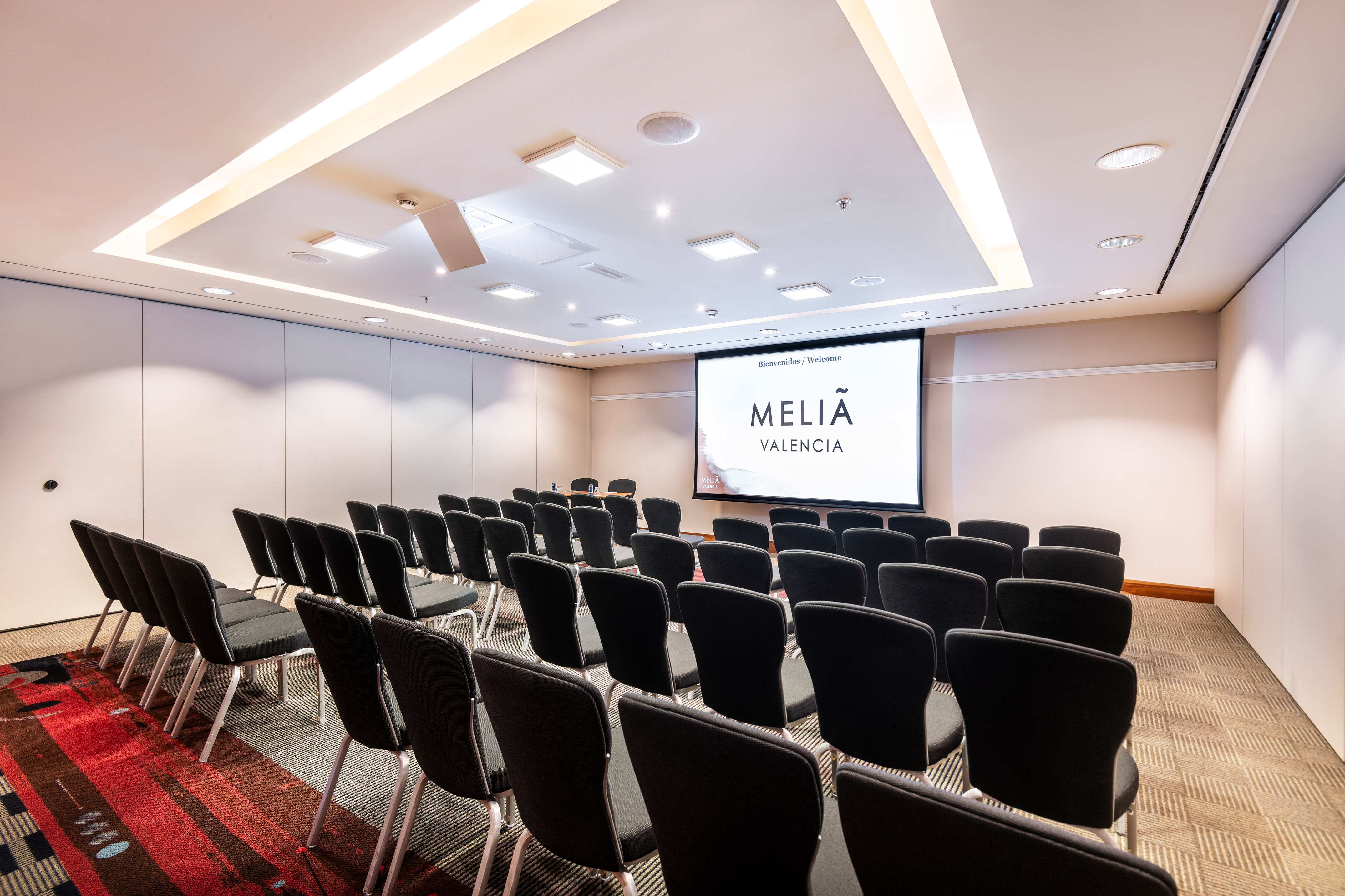Meliá Valencia modern conference room, rows of chairs, screen with hotel logo.