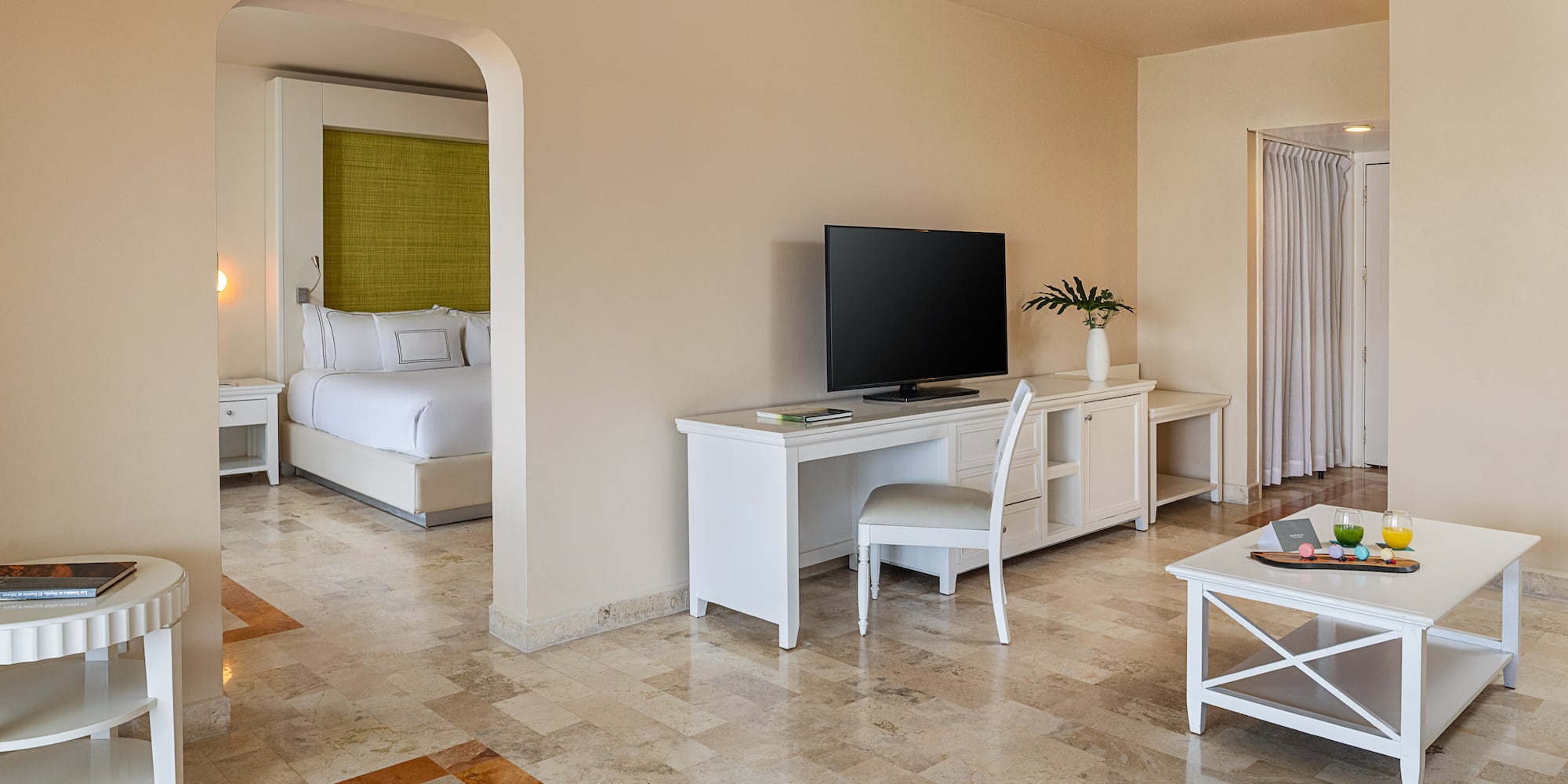 Bright hotel suite with living room, bedroom, TV, and modern tile floor.