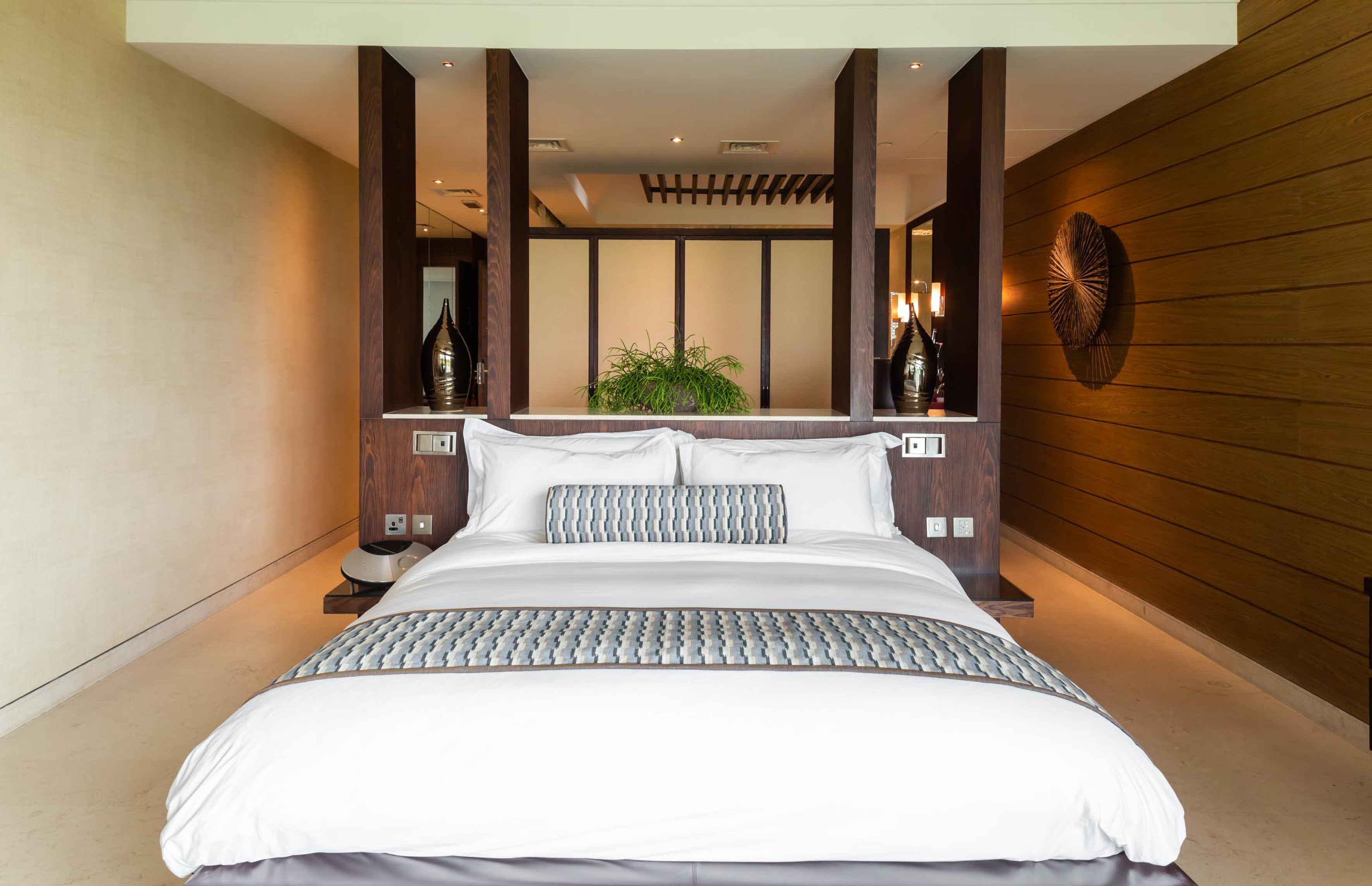 Modern luxury hotel bedroom with king bed, wood accents, and elegant decor.