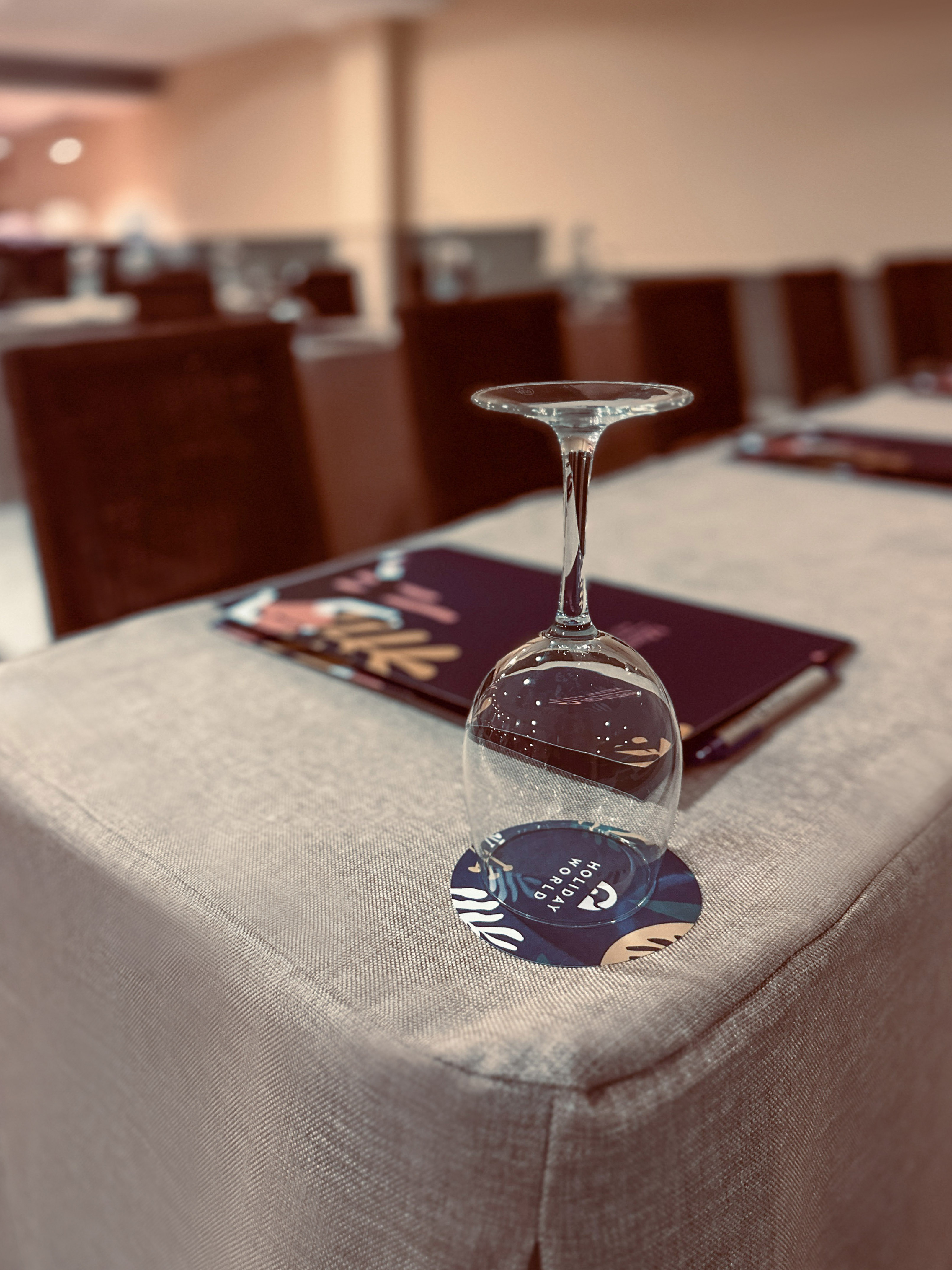 Empty wine glass on "Holiday World" coaster, menu on table. Conference setting.