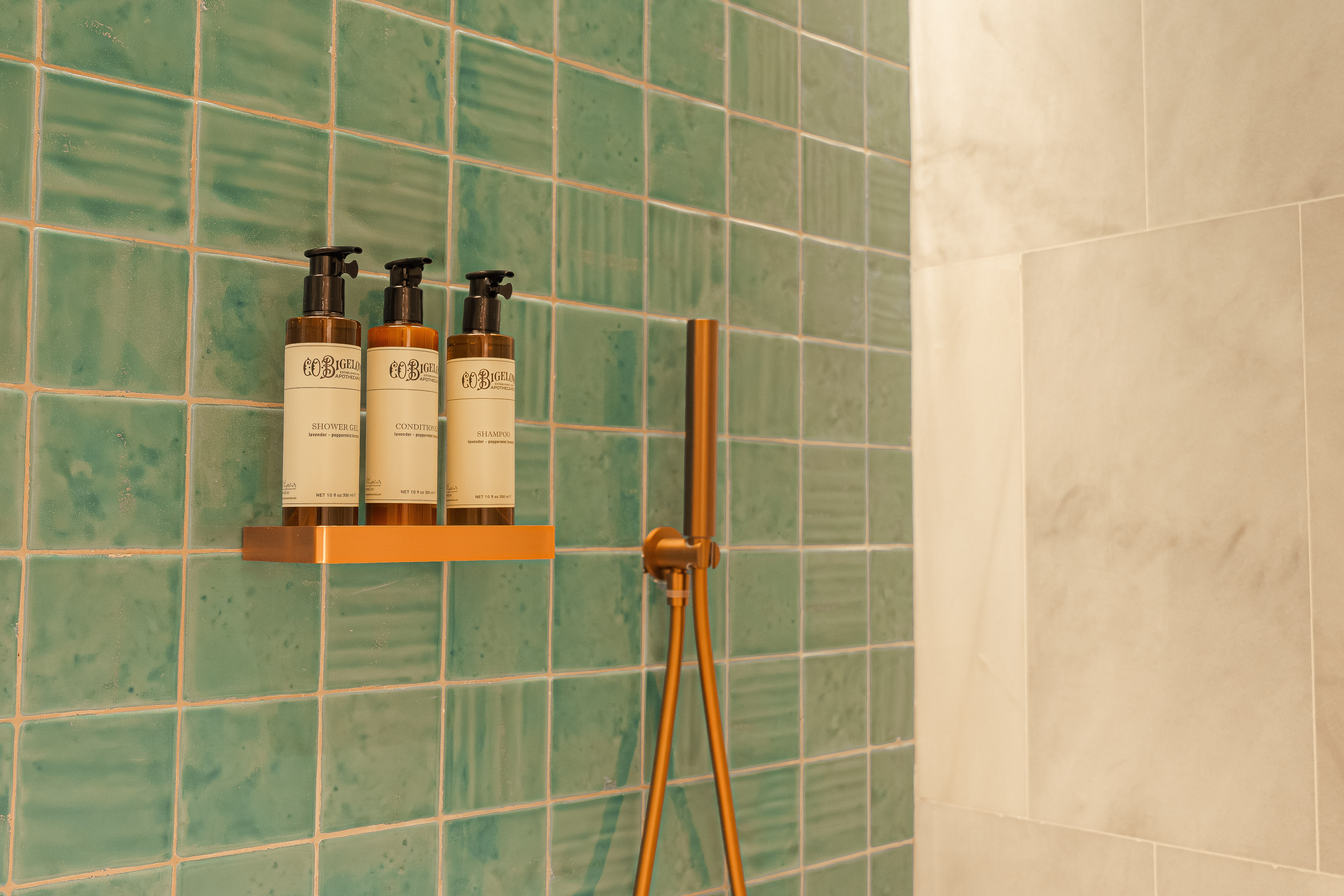 Modern green tiled shower with brass fixtures and C.O. Bigelow toiletries.