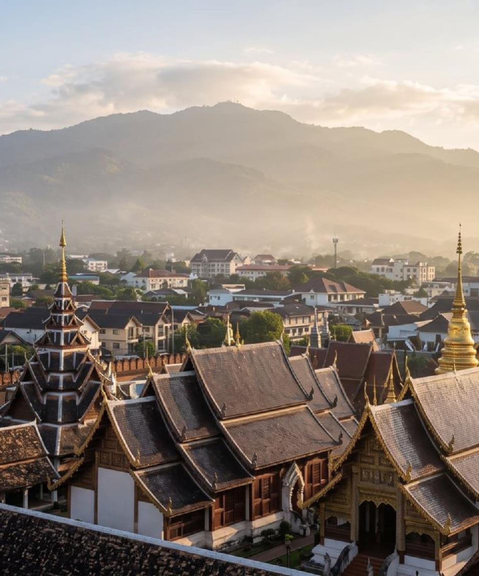 Golden-roofed temples, old city wall, Chiang Mai cityscape, hazy mountains.