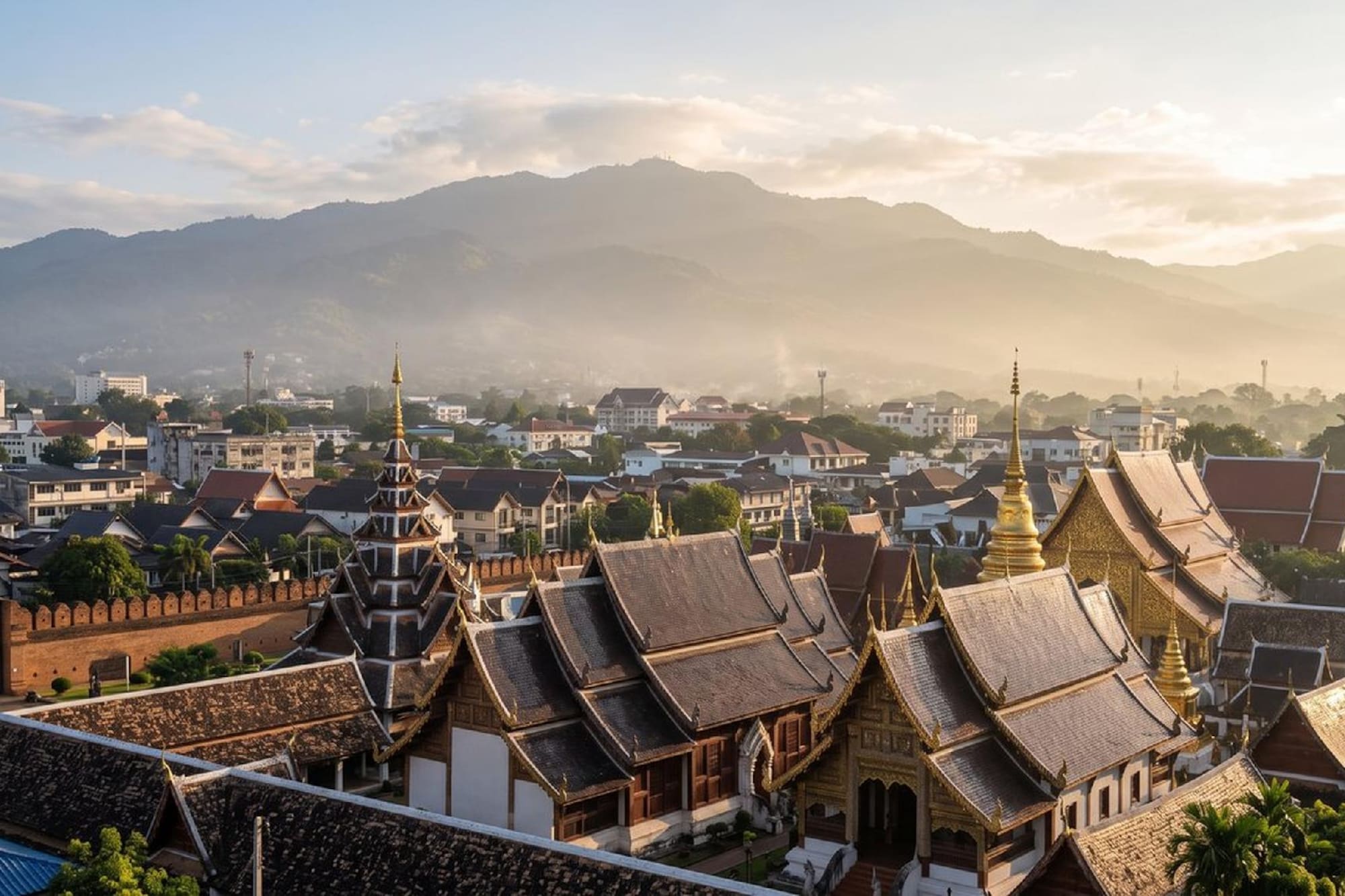 Golden-roofed temples, old city wall, Chiang Mai cityscape, hazy mountains.