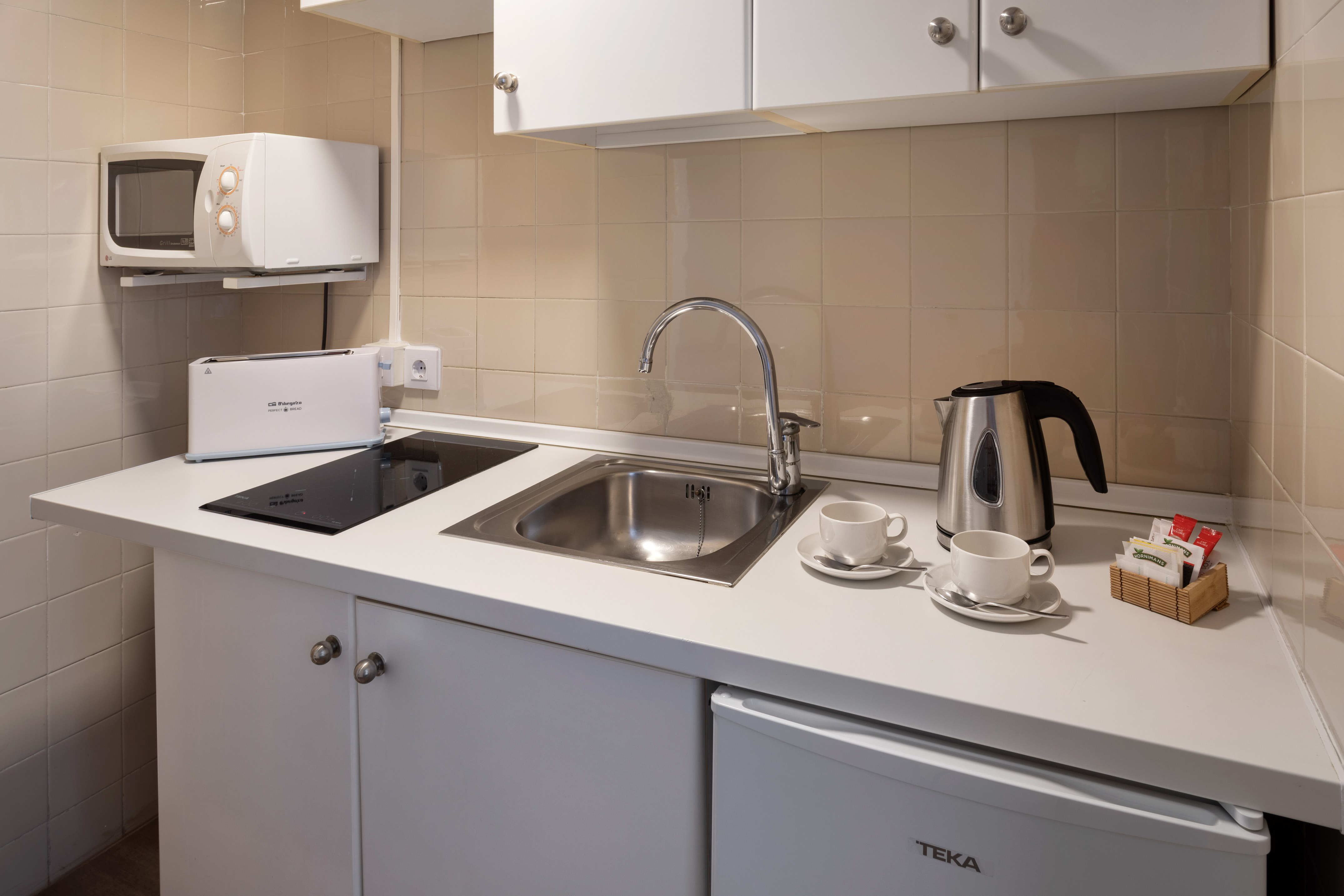 Small kitchenette with microwave, sink, induction hob, and kettle.