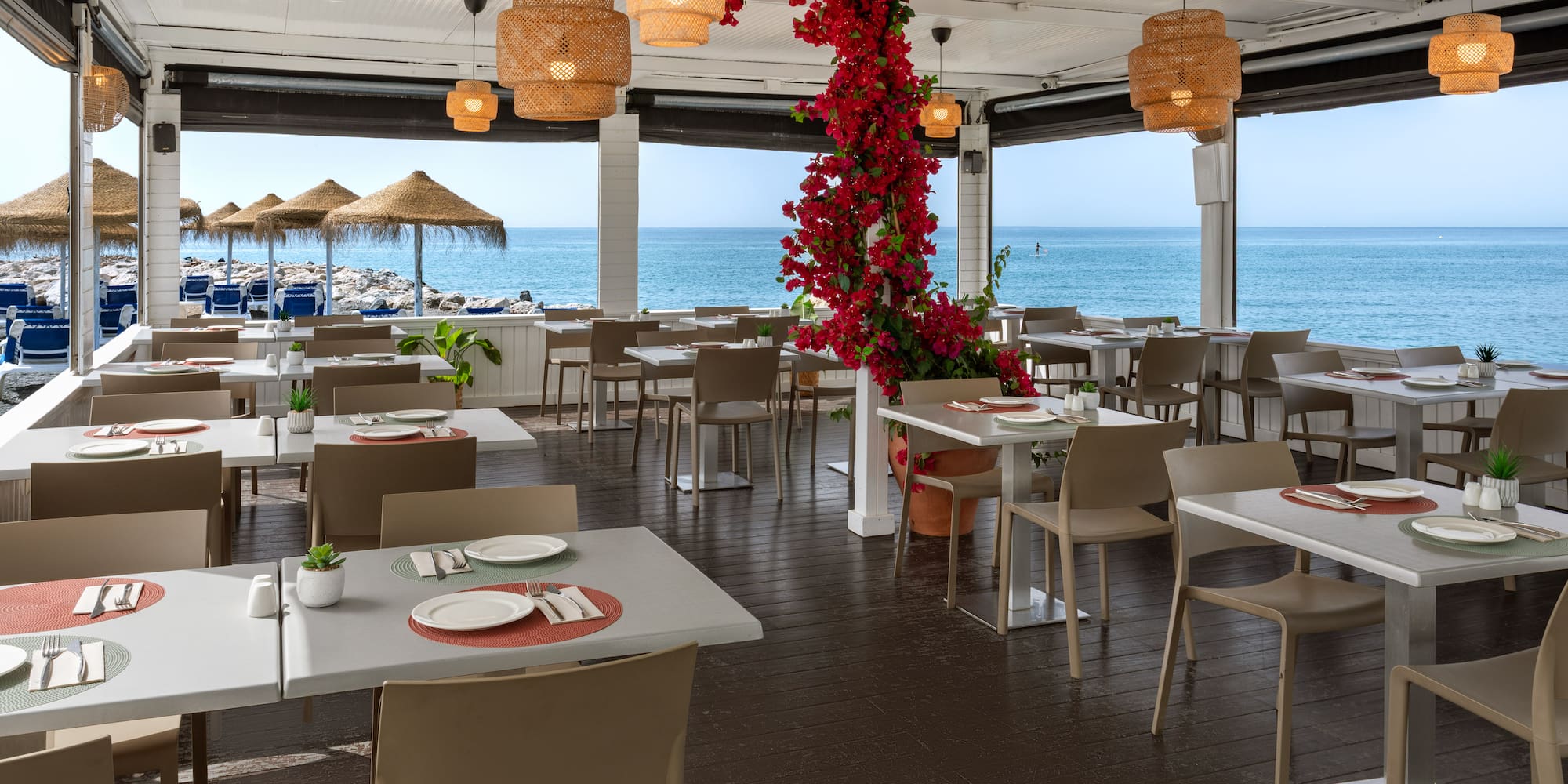 Beachfront restaurant with outdoor dining, sea view, and red bougainvillea.