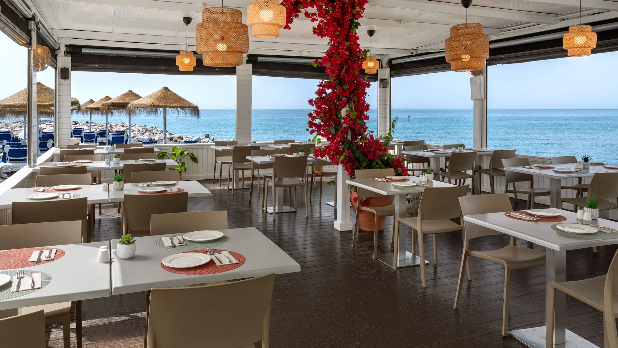 Beachfront restaurant with outdoor dining, sea view, and red bougainvillea.