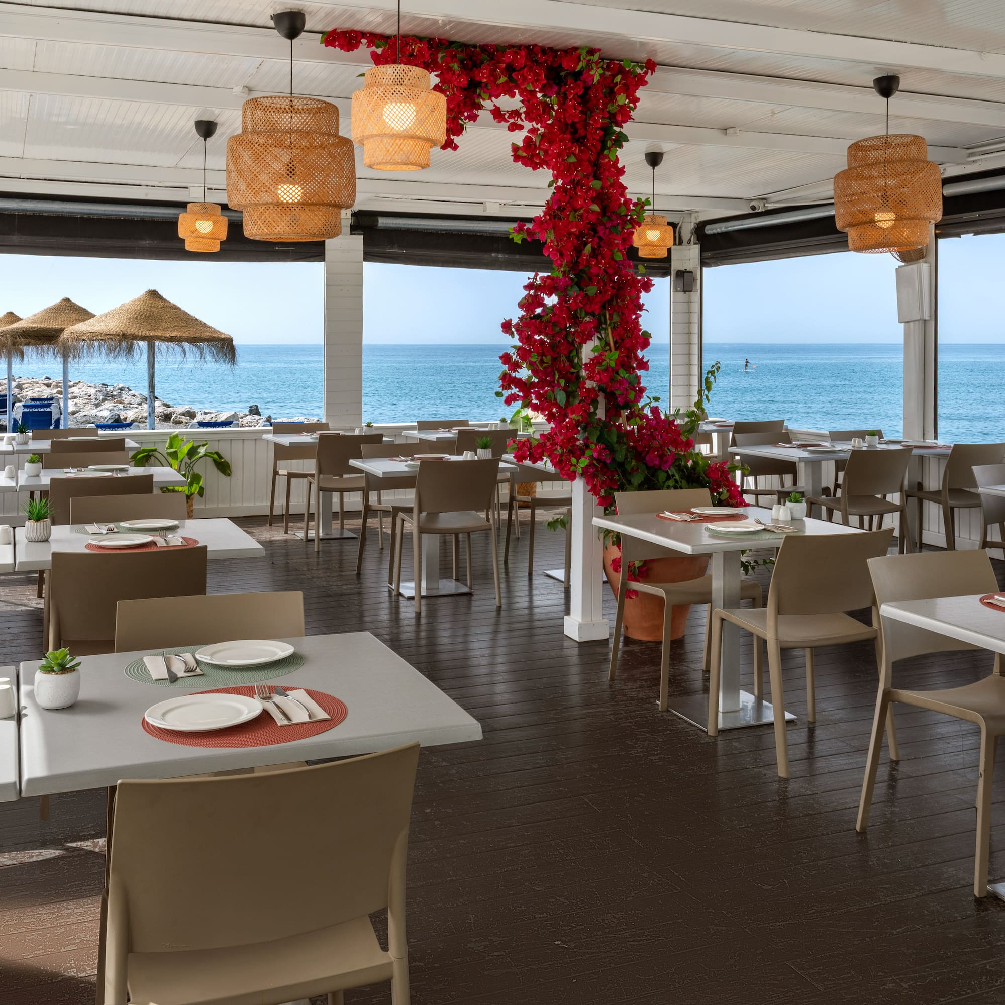 Beachfront restaurant with outdoor dining, sea view, and red bougainvillea.