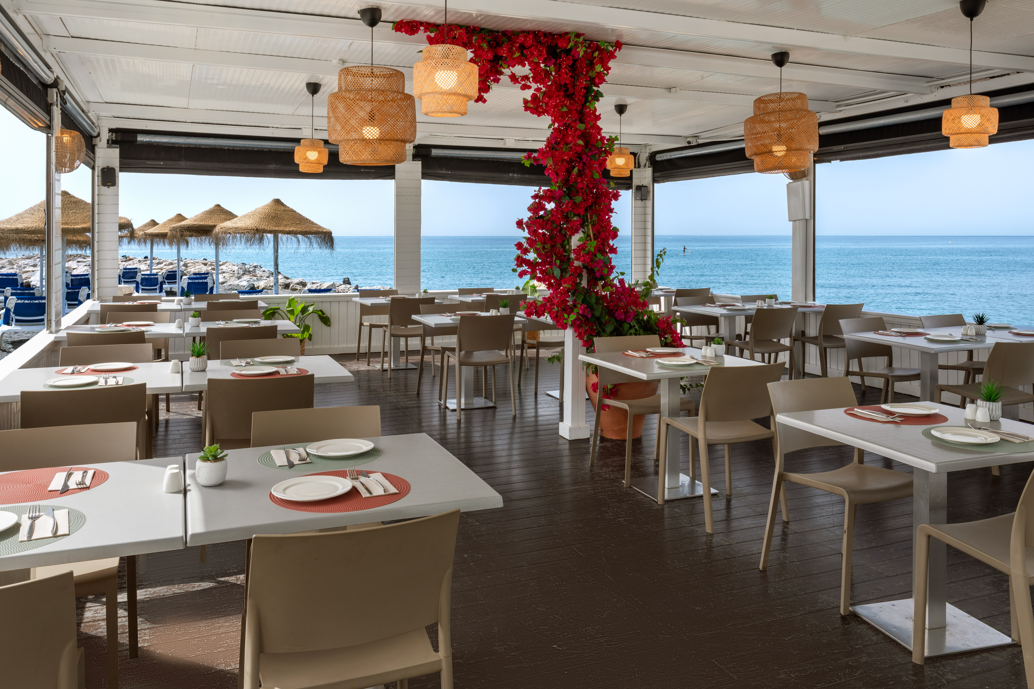 Beachfront restaurant with outdoor dining, sea view, and red bougainvillea.