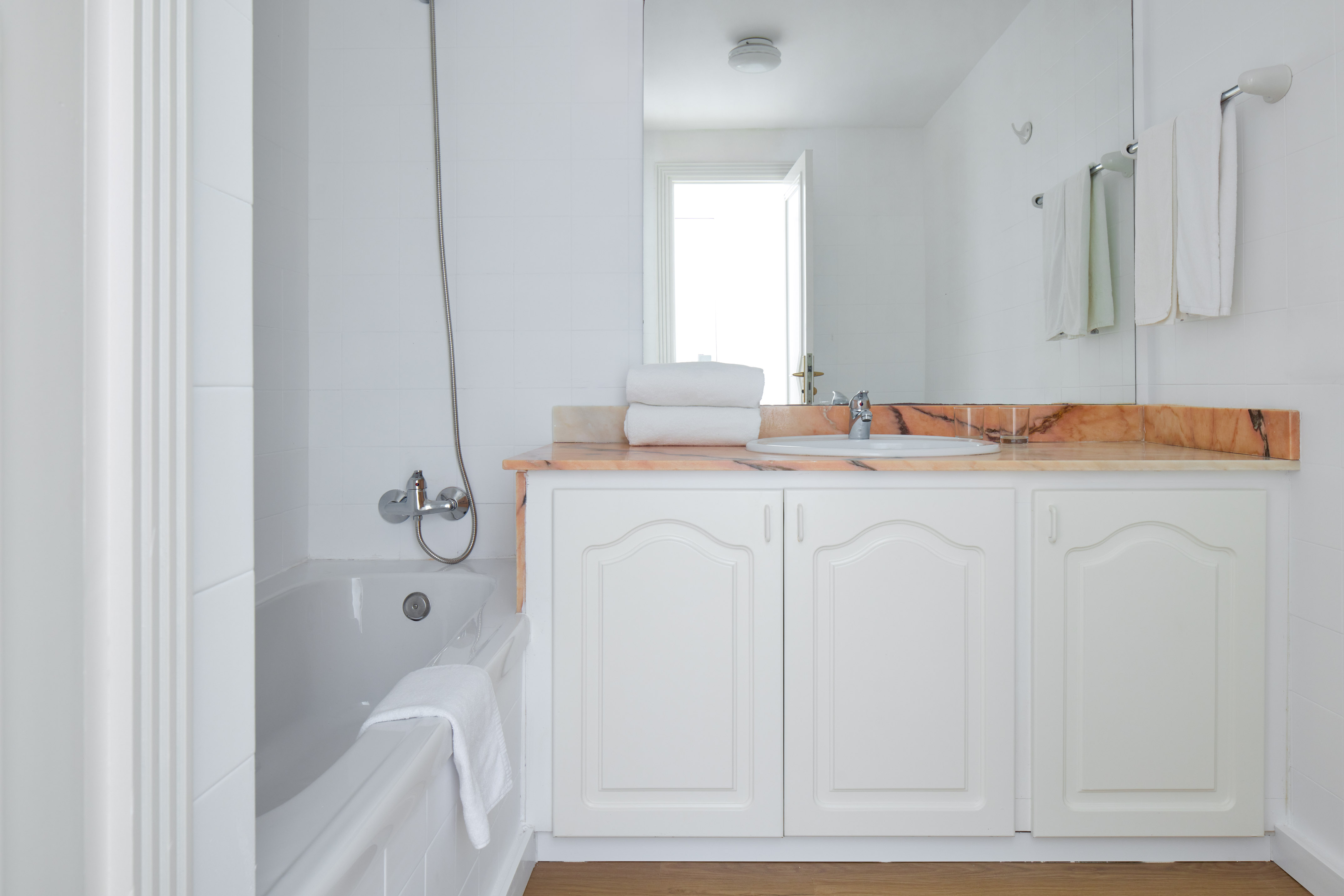 White bathroom with bathtub, shower, vanity, sink, and marble counter.