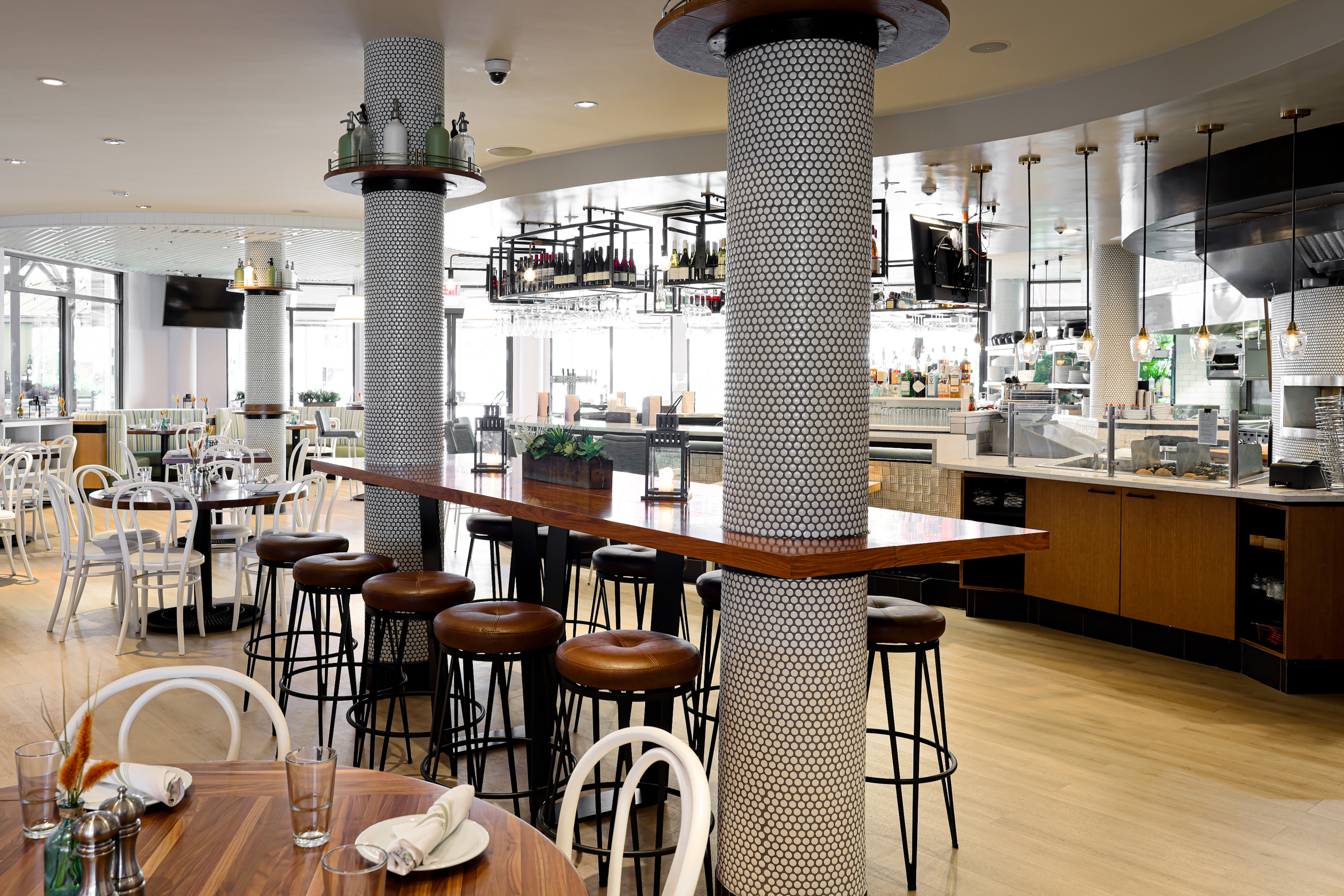 Modern restaurant interior: communal wood table, leather stools, tiled columns.