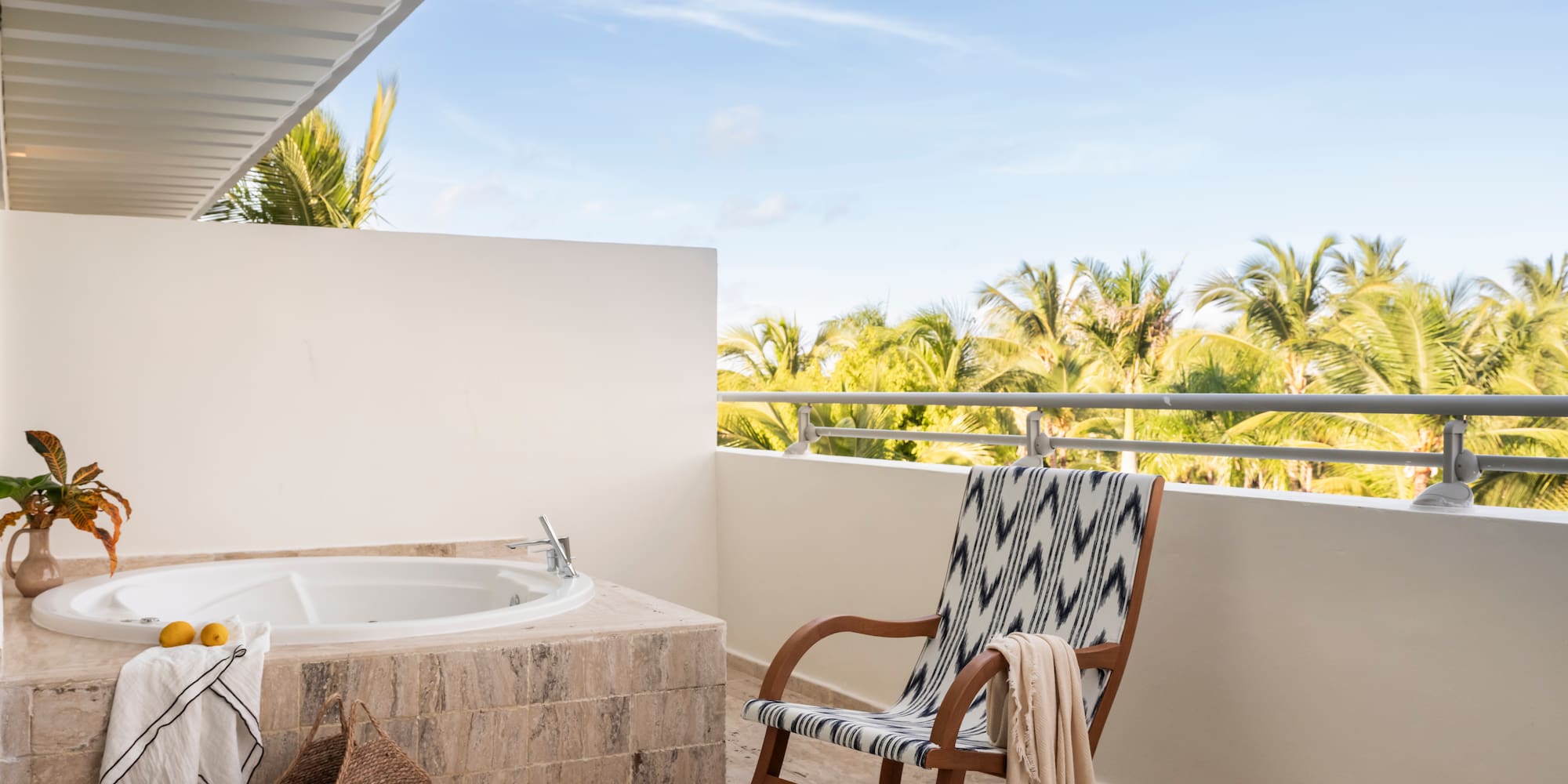 Outdoor balcony with jacuzzi, rocking chair, and tropical palm tree view.