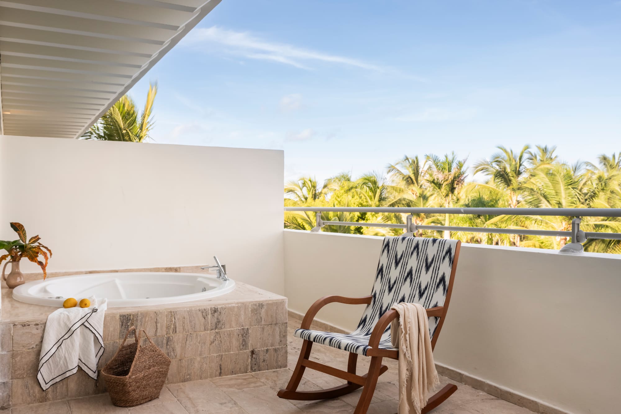 Outdoor balcony with jacuzzi, rocking chair, and tropical palm tree view.