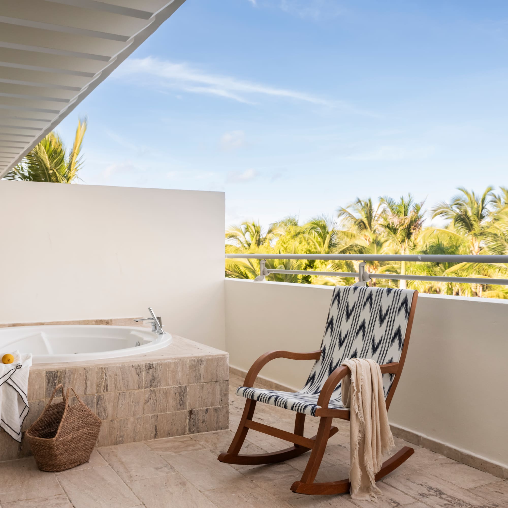 Outdoor balcony with jacuzzi, rocking chair, and tropical palm tree view.
