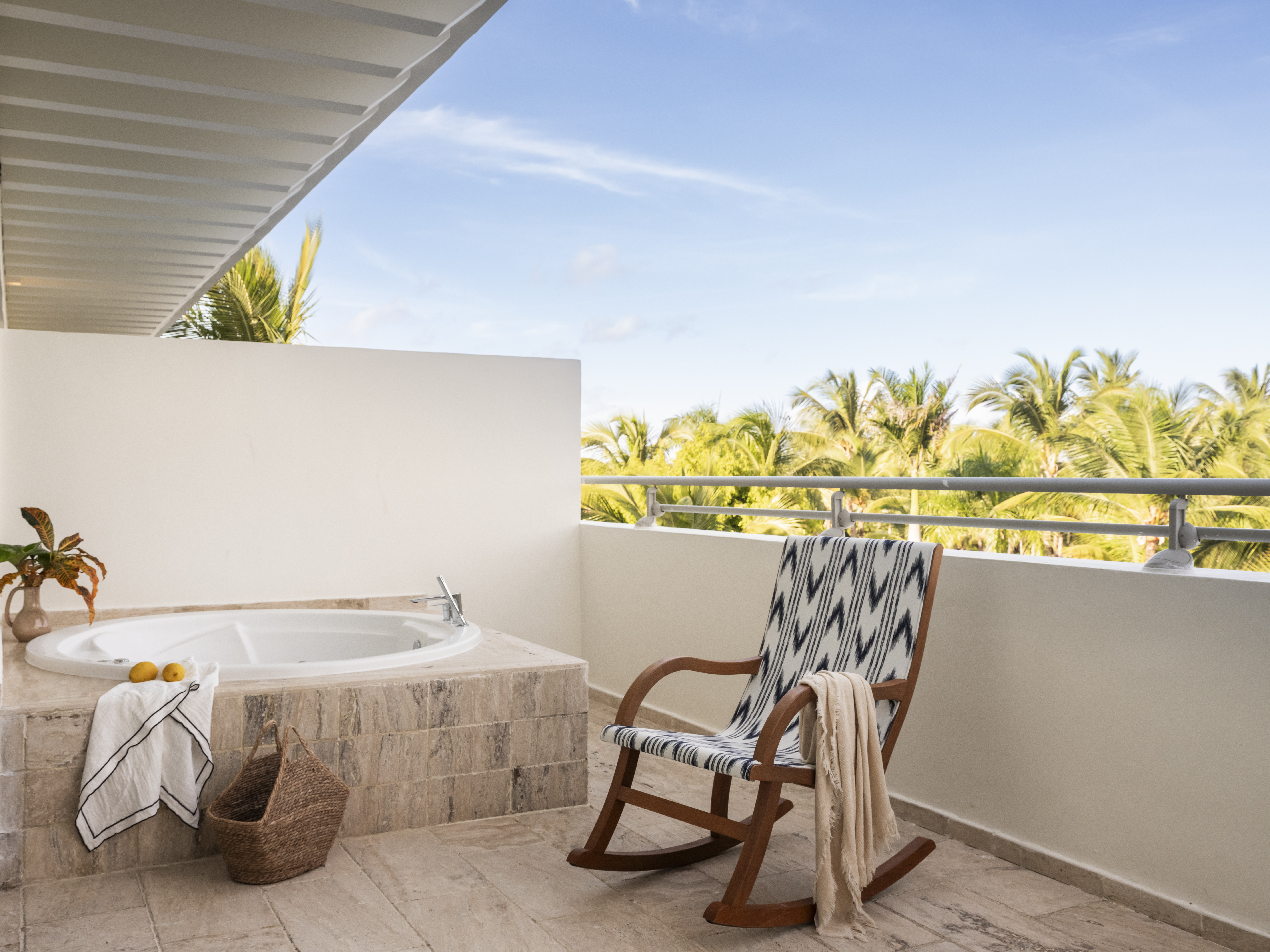 Outdoor balcony with jacuzzi, rocking chair, and tropical palm tree view.