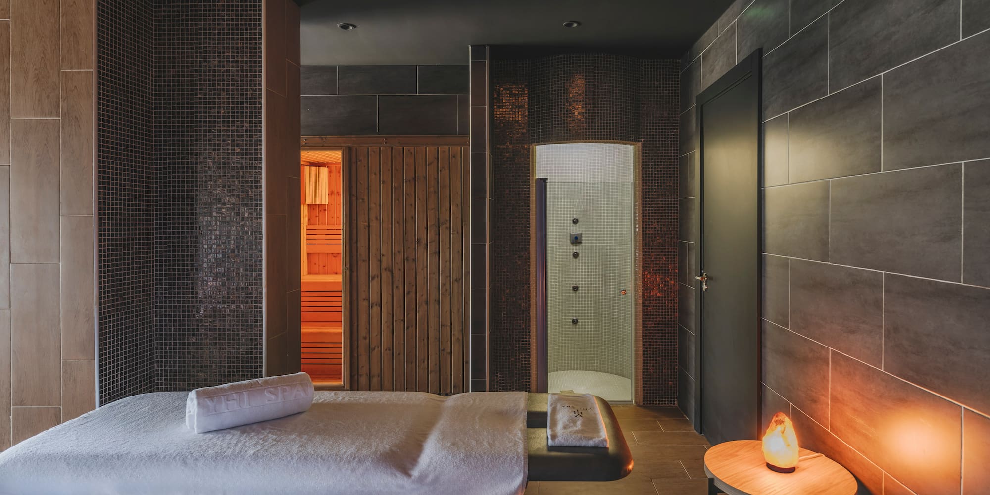 Modern spa room with two massage beds, sauna, shower, and salt lamp.