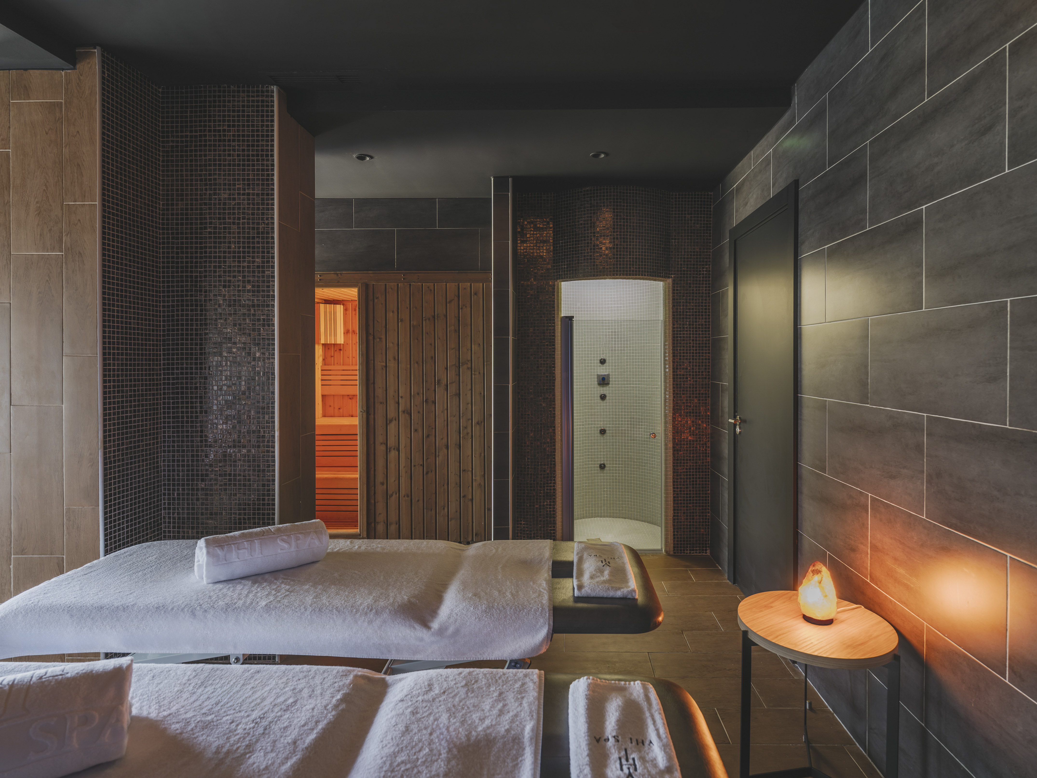 Modern spa room with two massage beds, sauna, shower, and salt lamp.