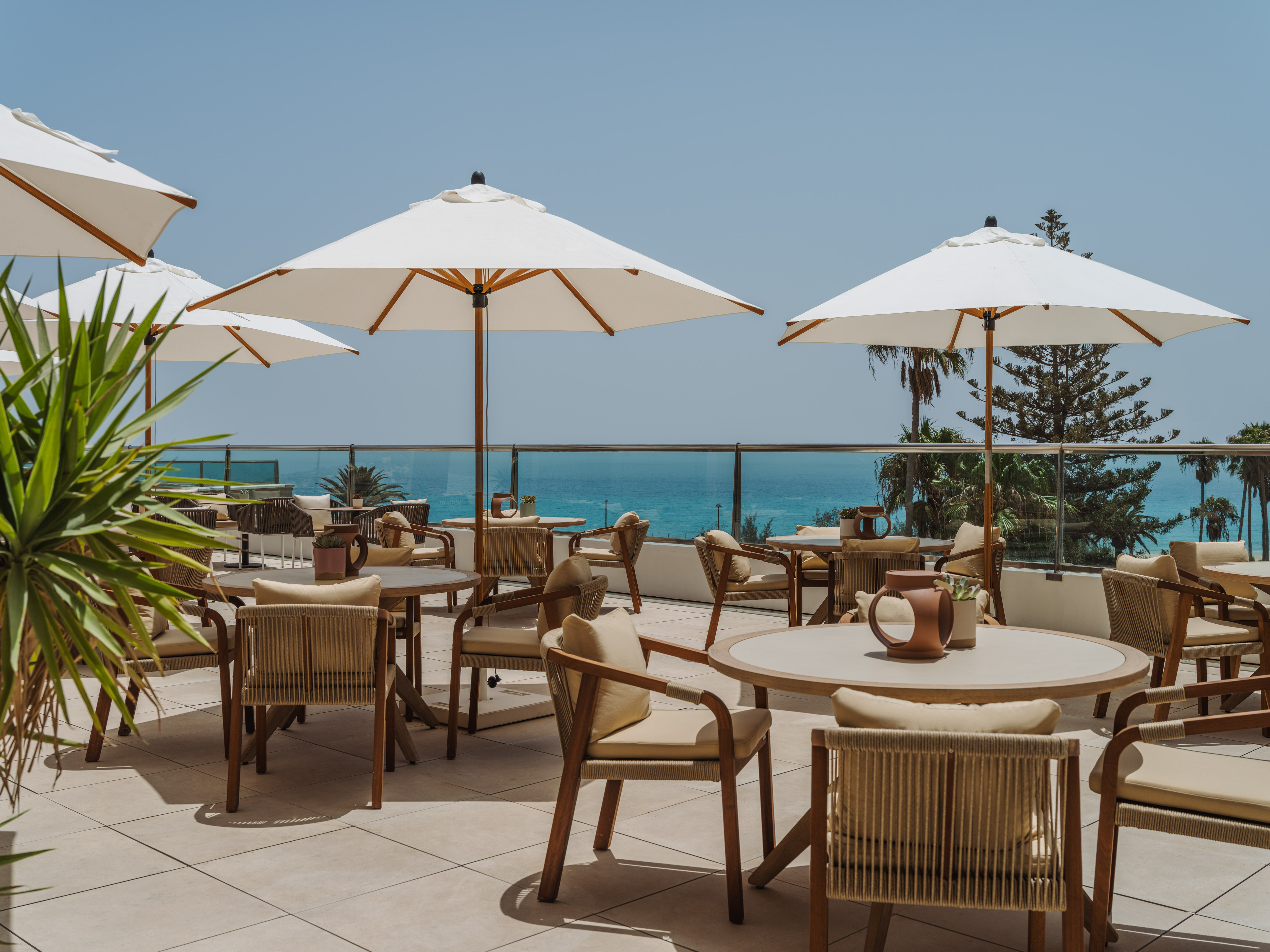 Hotel terrace with ocean view dining, white umbrellas, and comfortable chairs.
