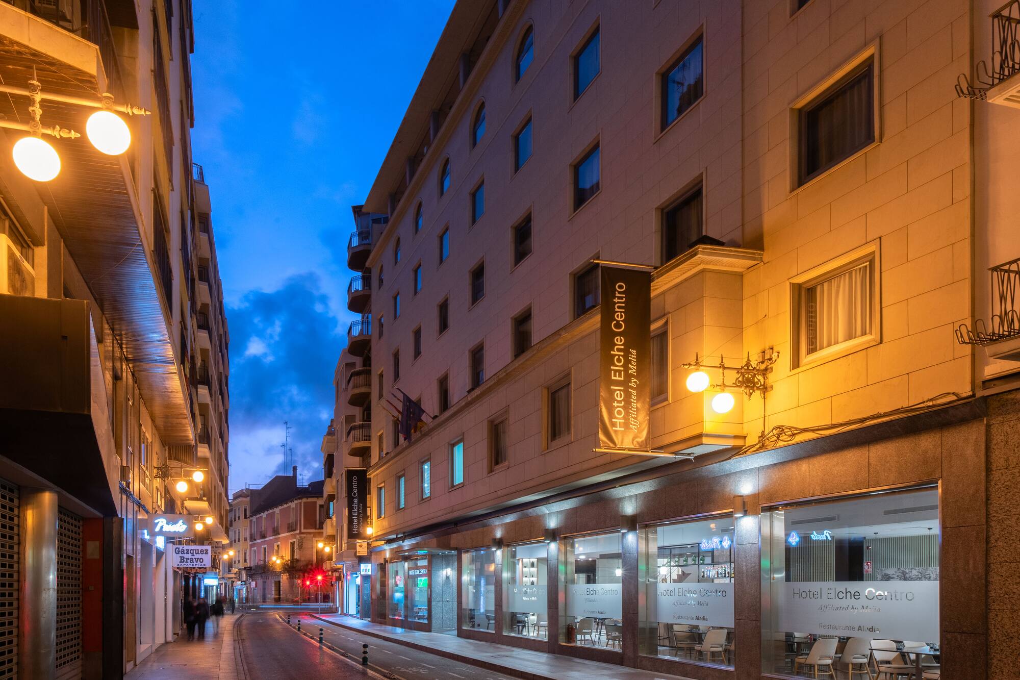 Hotel Elche Centro by Meliá at dusk on a city street, illuminated building facade.
