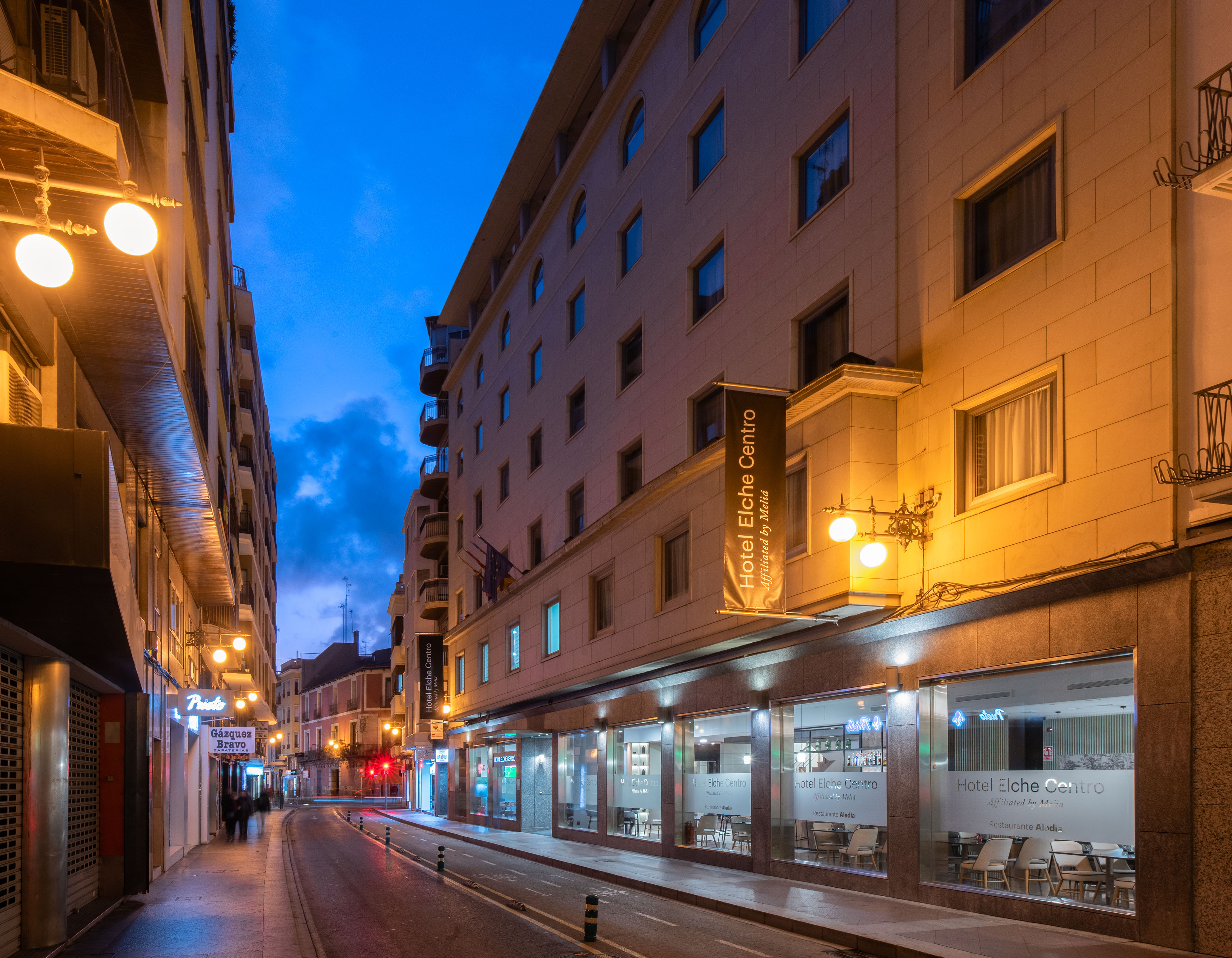 Hotel Elche Centro by Meliá at dusk on a city street, illuminated building facade.