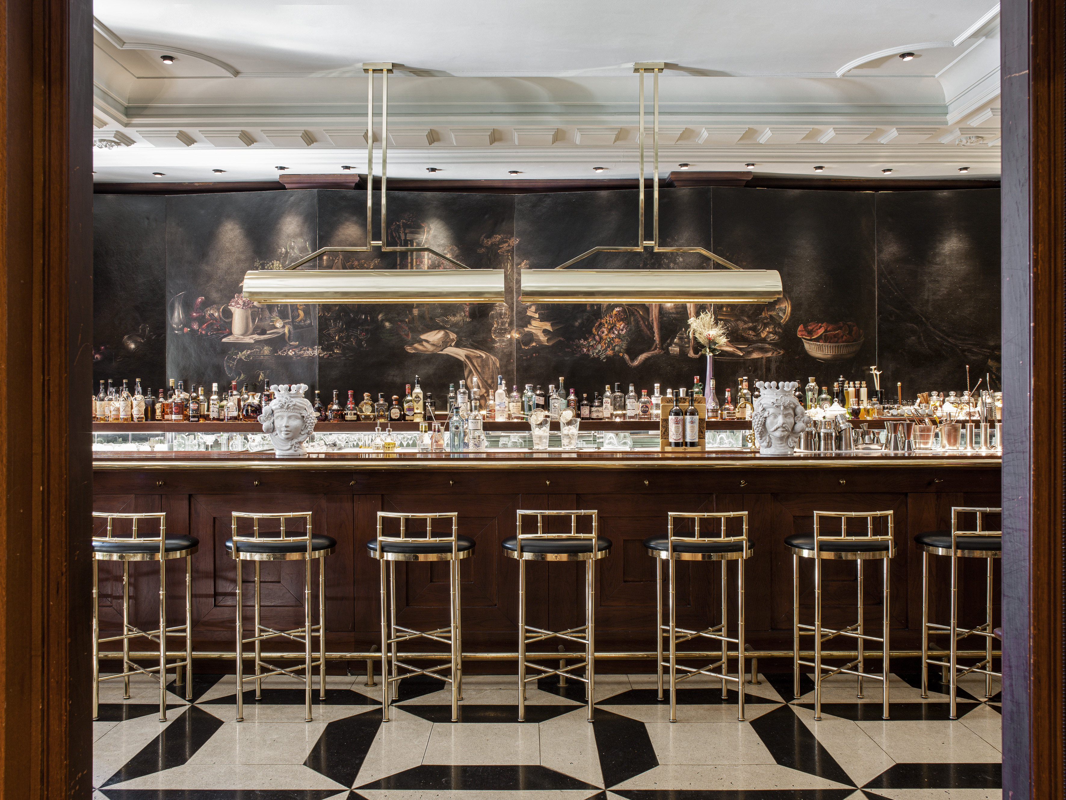 Elegant cocktail bar: dark wood, gold stools, still life mural, checkered floor.