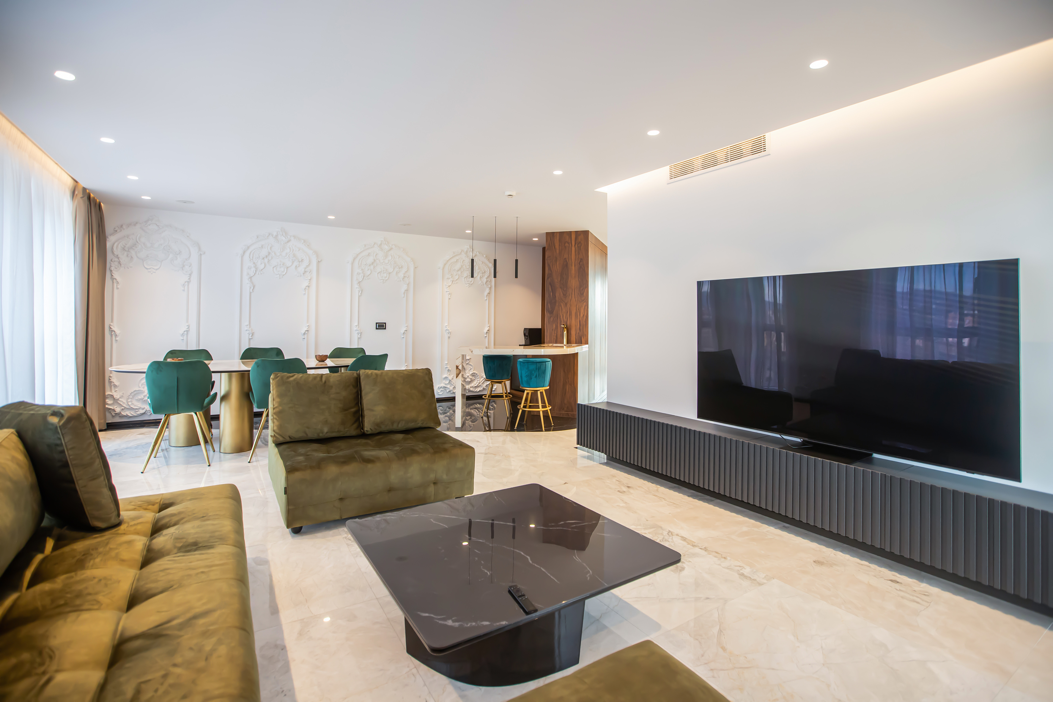Modern open concept living room with olive sofas, dining area, and kitchenette.