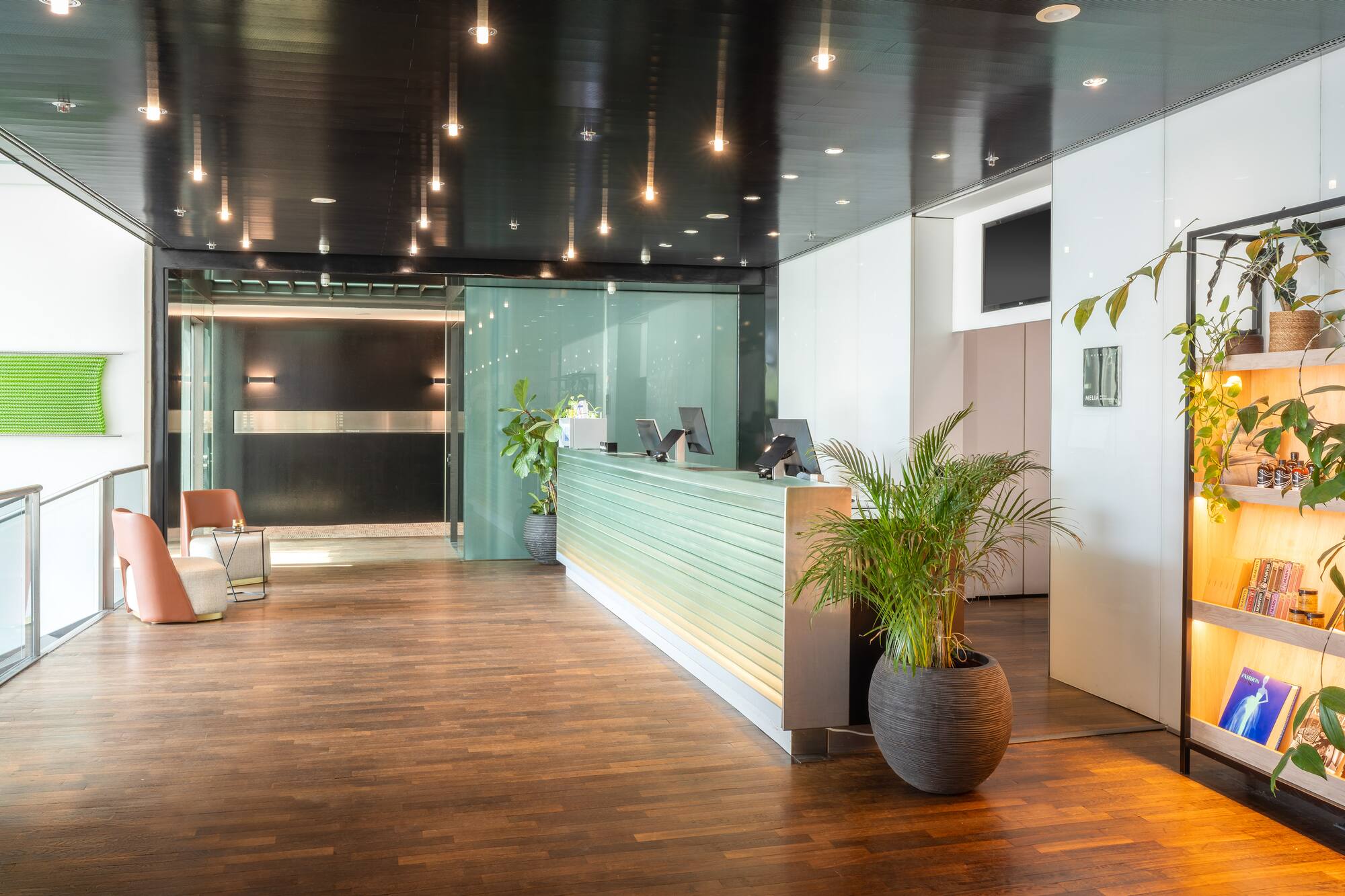 Modern reception lobby with glowing desk, wood floor, and green potted plants.
