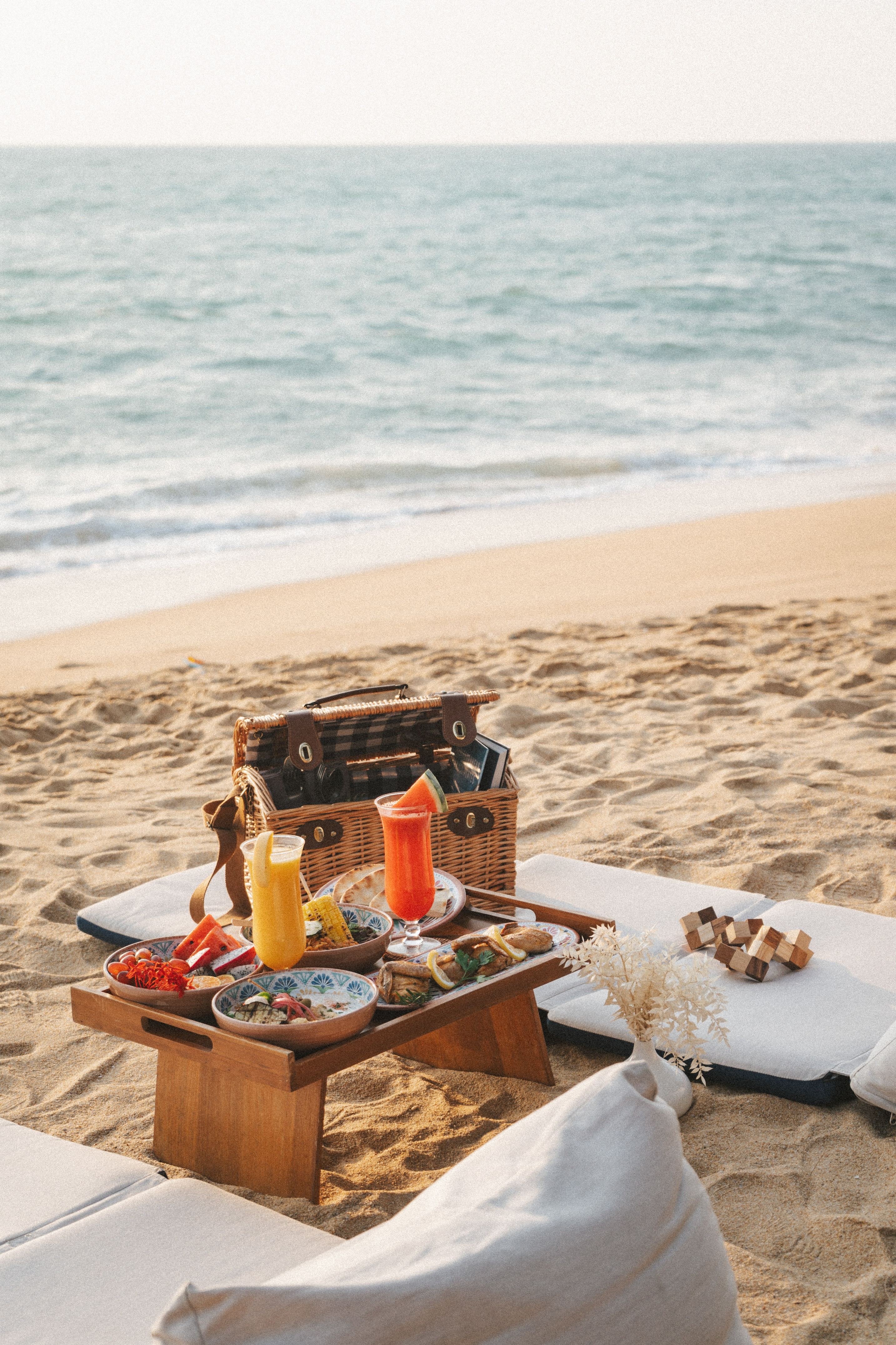 Outdoor beach picnic with colorful food, juices, and basket by the ocean.