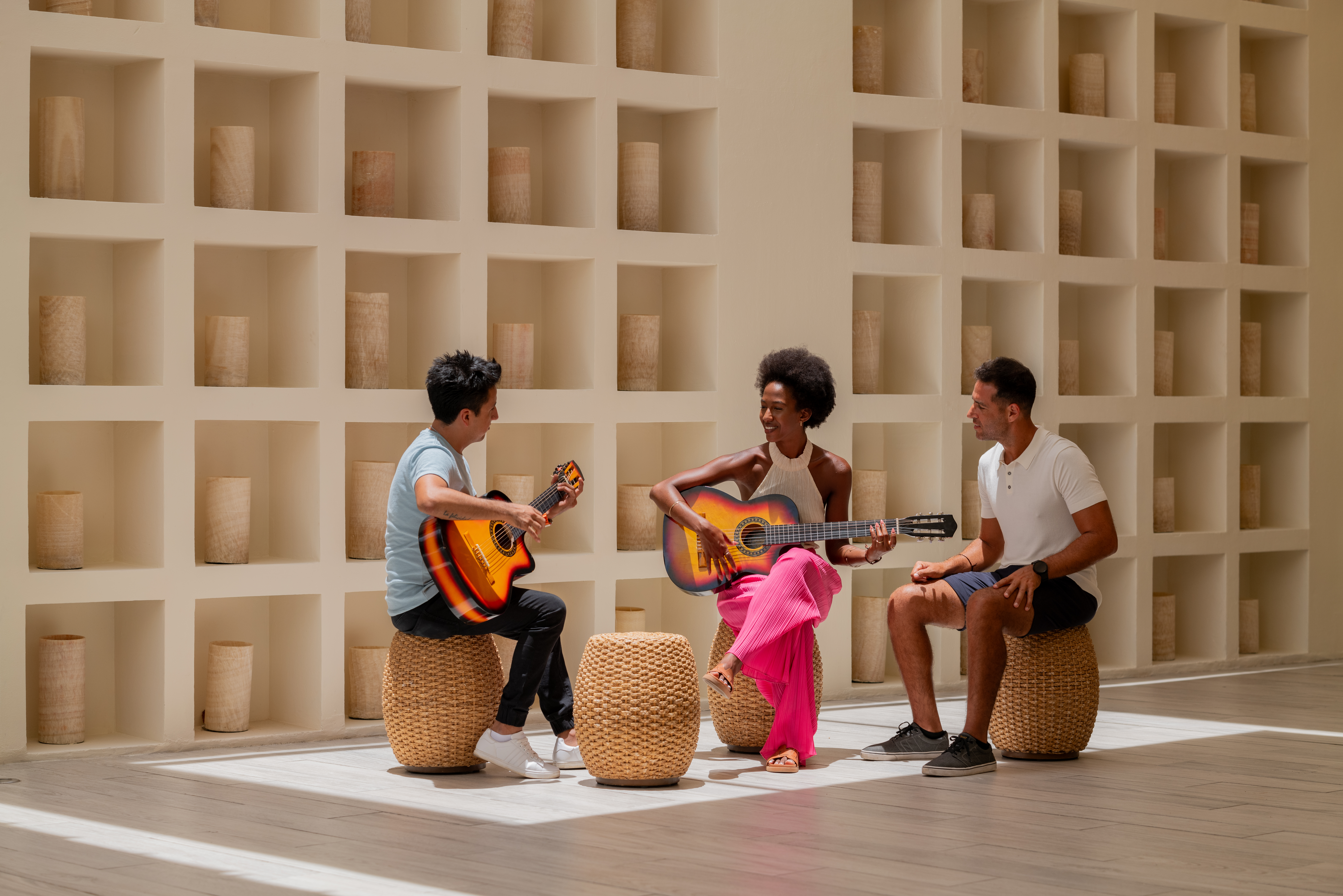 Two people playing acoustic guitars while a third listens, in a modern lobby.