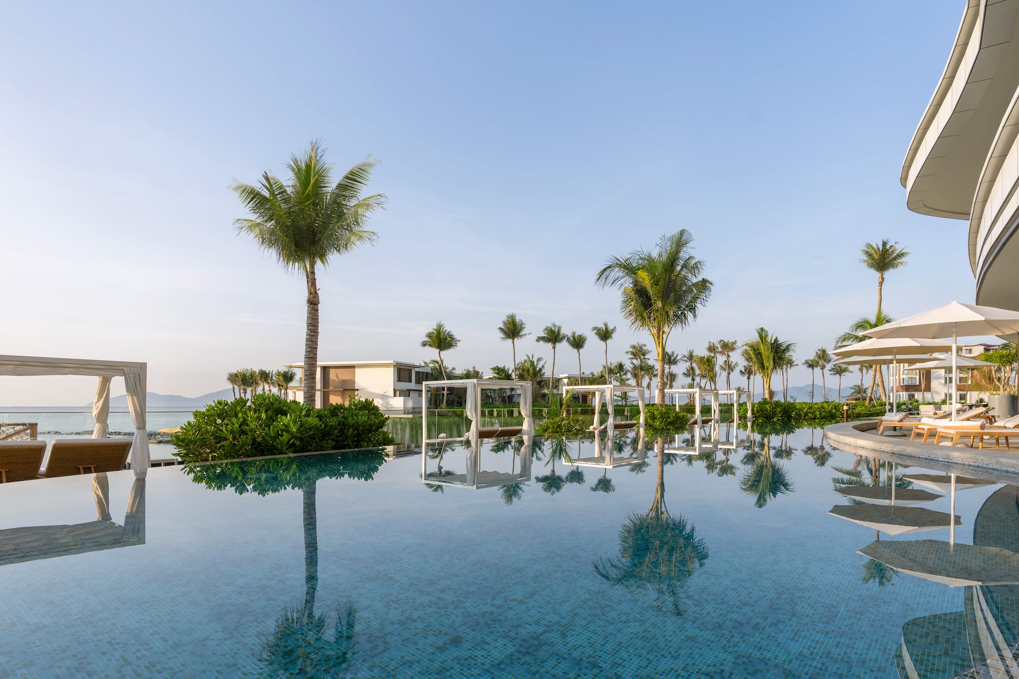 Tropical resort infinity pool with palm trees, ocean view, and luxury daybeds.
