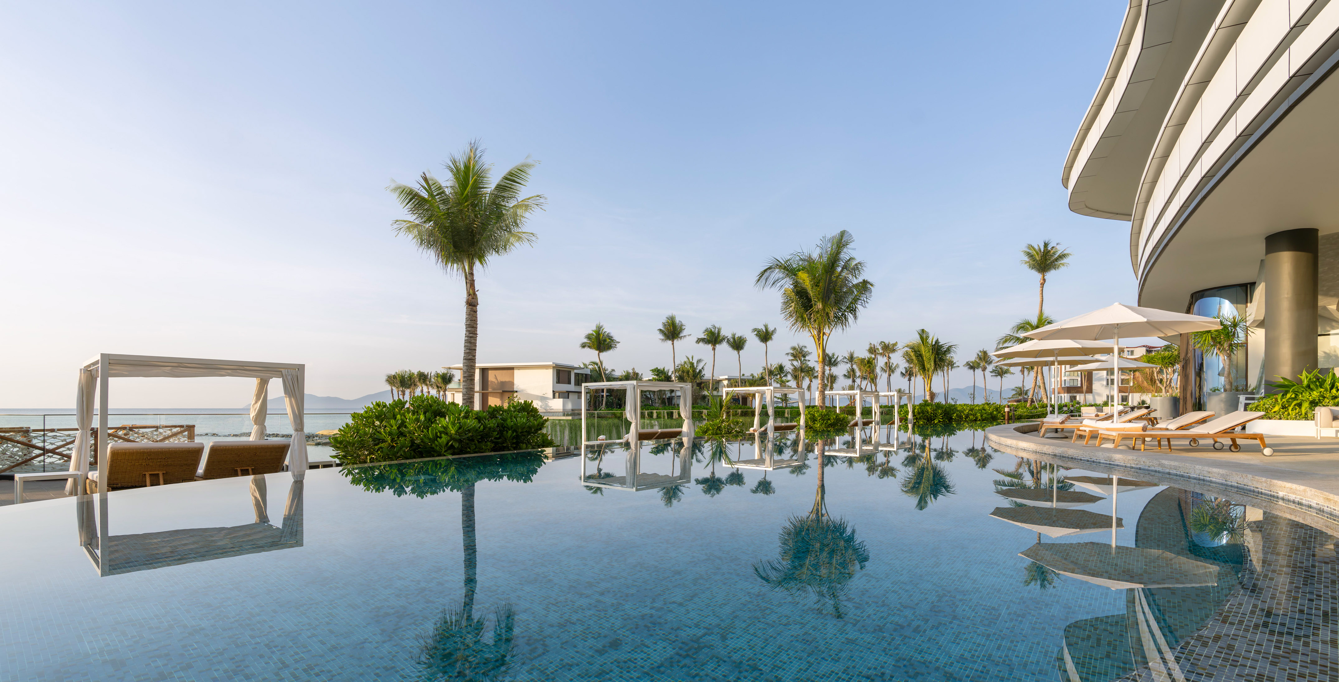 Tropical resort infinity pool with palm trees, ocean view, and luxury daybeds.