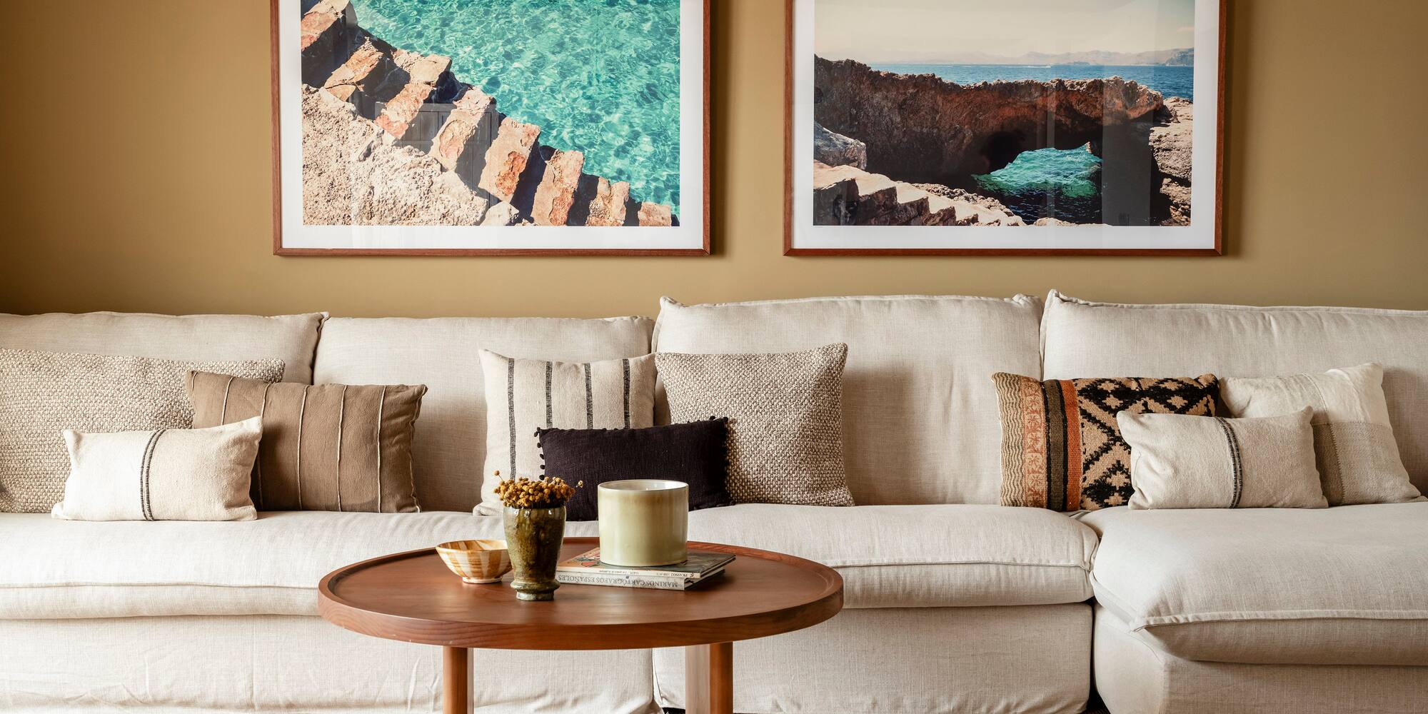 a couch with pillows and a coffee table with two framed pictures on the wall