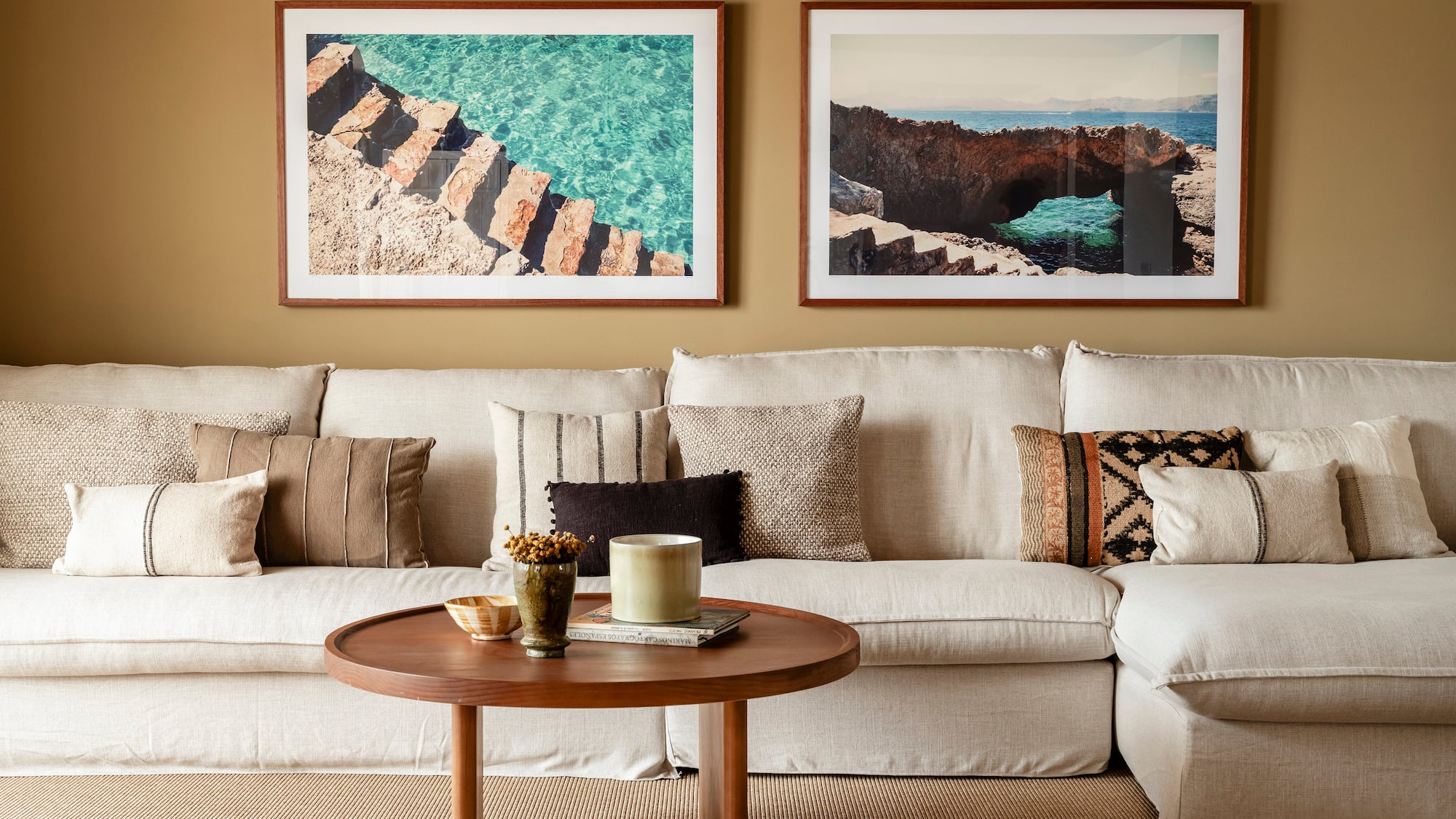 a couch with pillows and a coffee table with two framed pictures on the wall