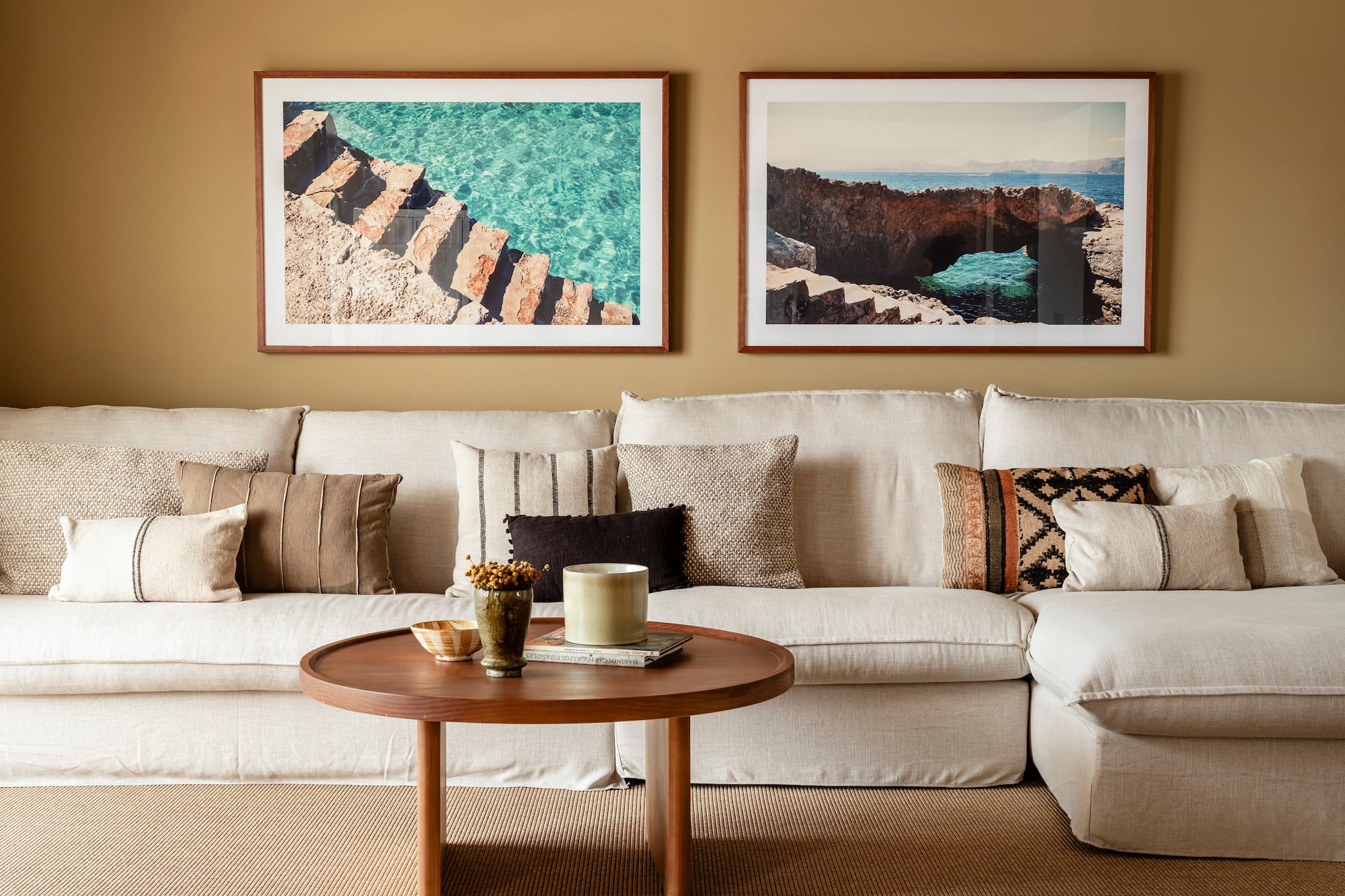 a couch with pillows and a coffee table with two framed pictures on the wall