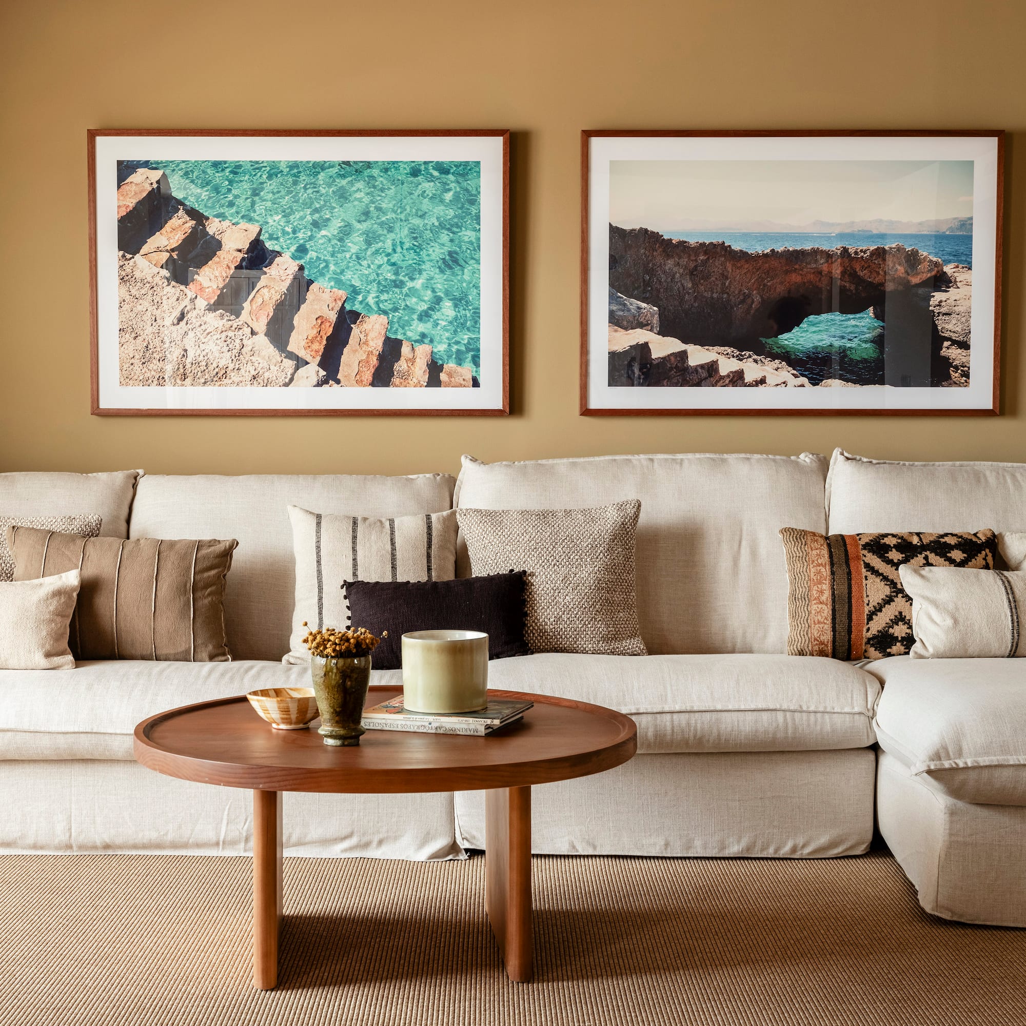 a couch with pillows and a coffee table with two framed pictures on the wall