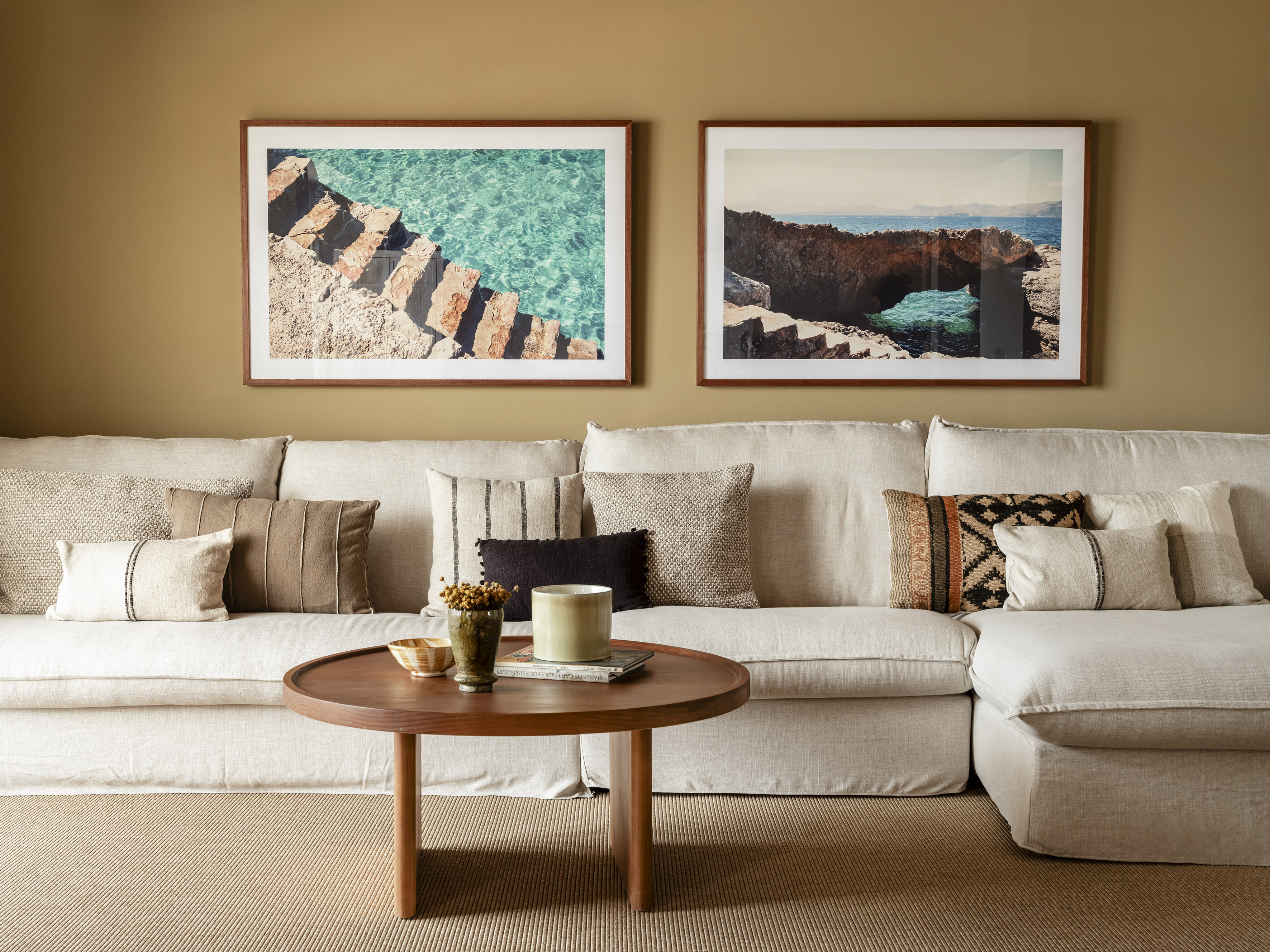 a couch with pillows and a coffee table with two framed pictures on the wall