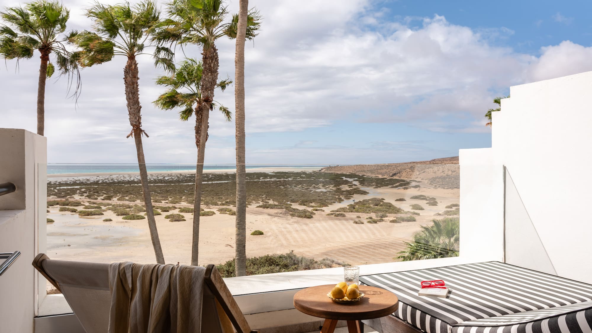 Ocean view balcony with palm trees, beach, and lounge furniture.