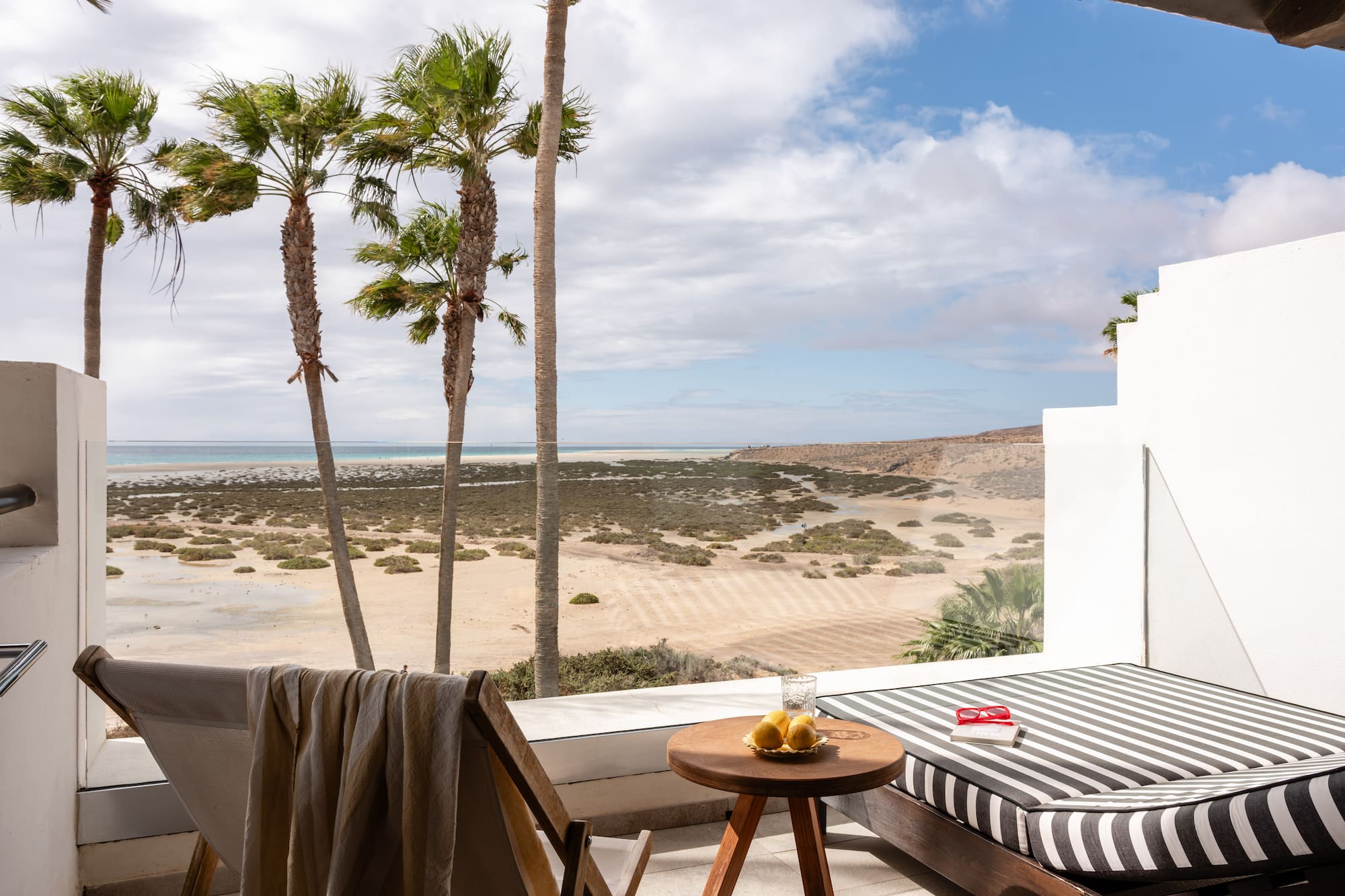 Ocean view balcony with palm trees, beach, and lounge furniture.