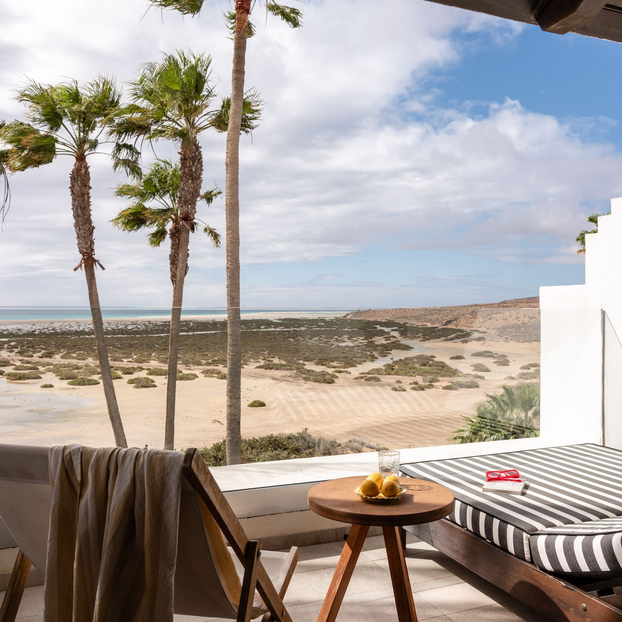 Ocean view balcony with palm trees, beach, and lounge furniture.
