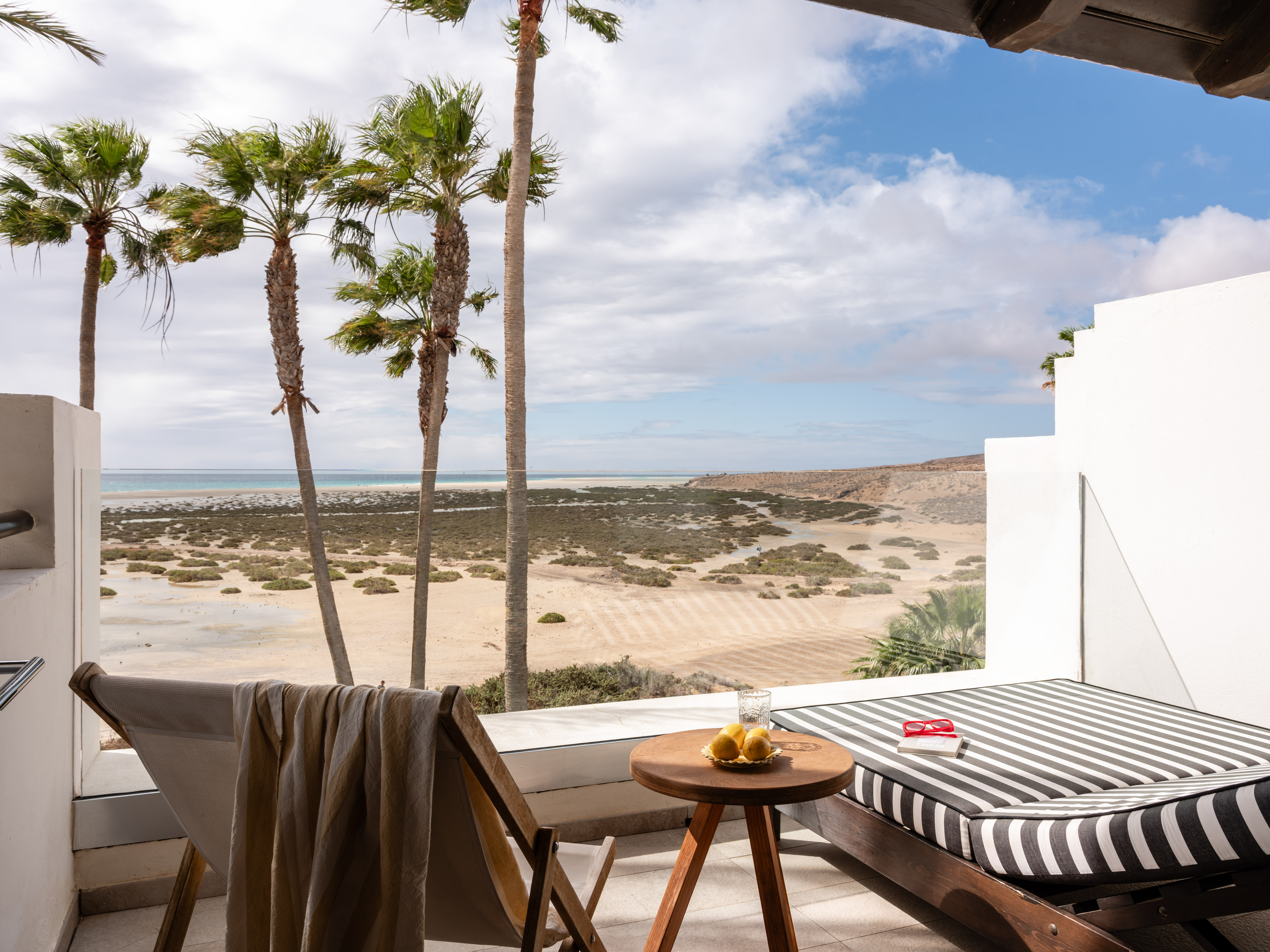 Ocean view balcony with palm trees, beach, and lounge furniture.