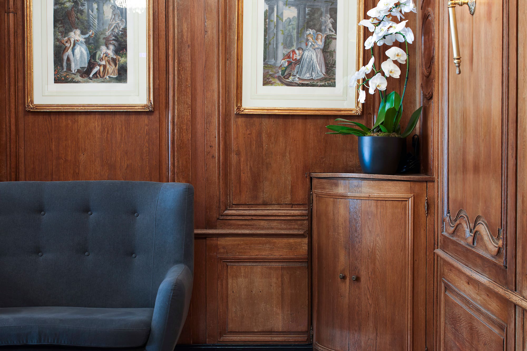 Elegant foyer with wood paneling, classical art, grey sofa, and marble floor.