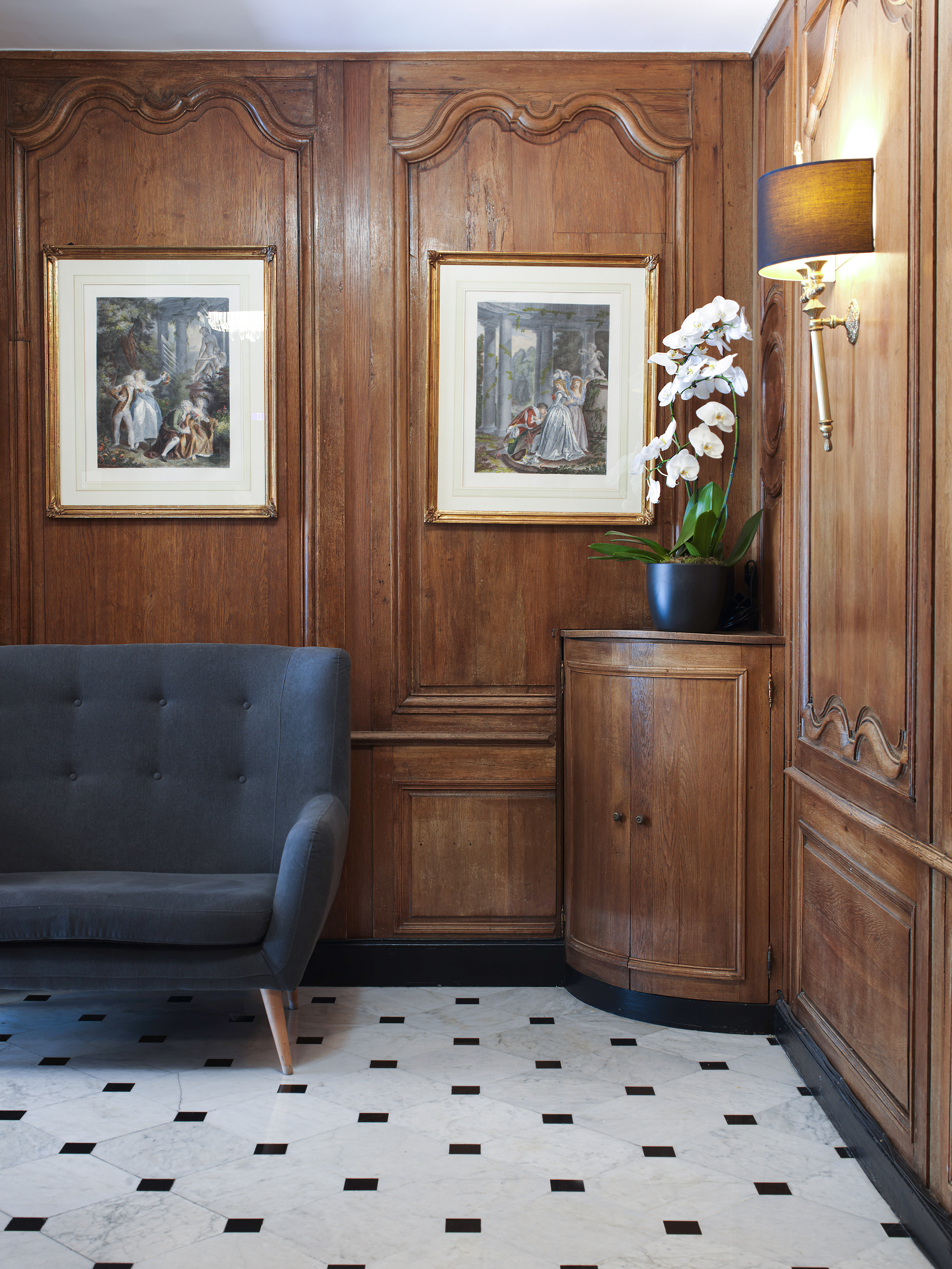 Elegant foyer with wood paneling, classical art, grey sofa, and marble floor.
