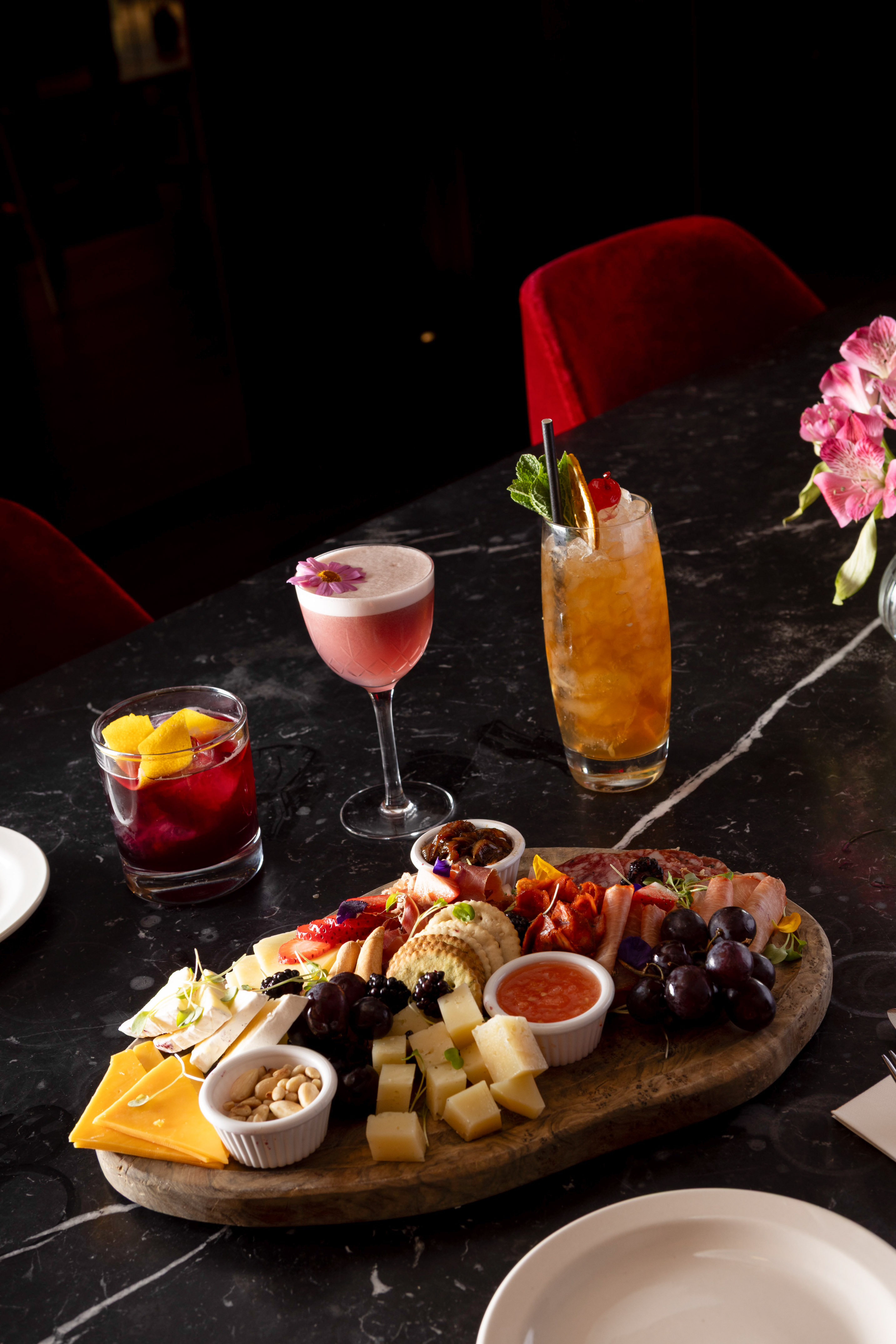 Charcuterie board with cheese, meats, grapes, crackers, and colorful cocktails.