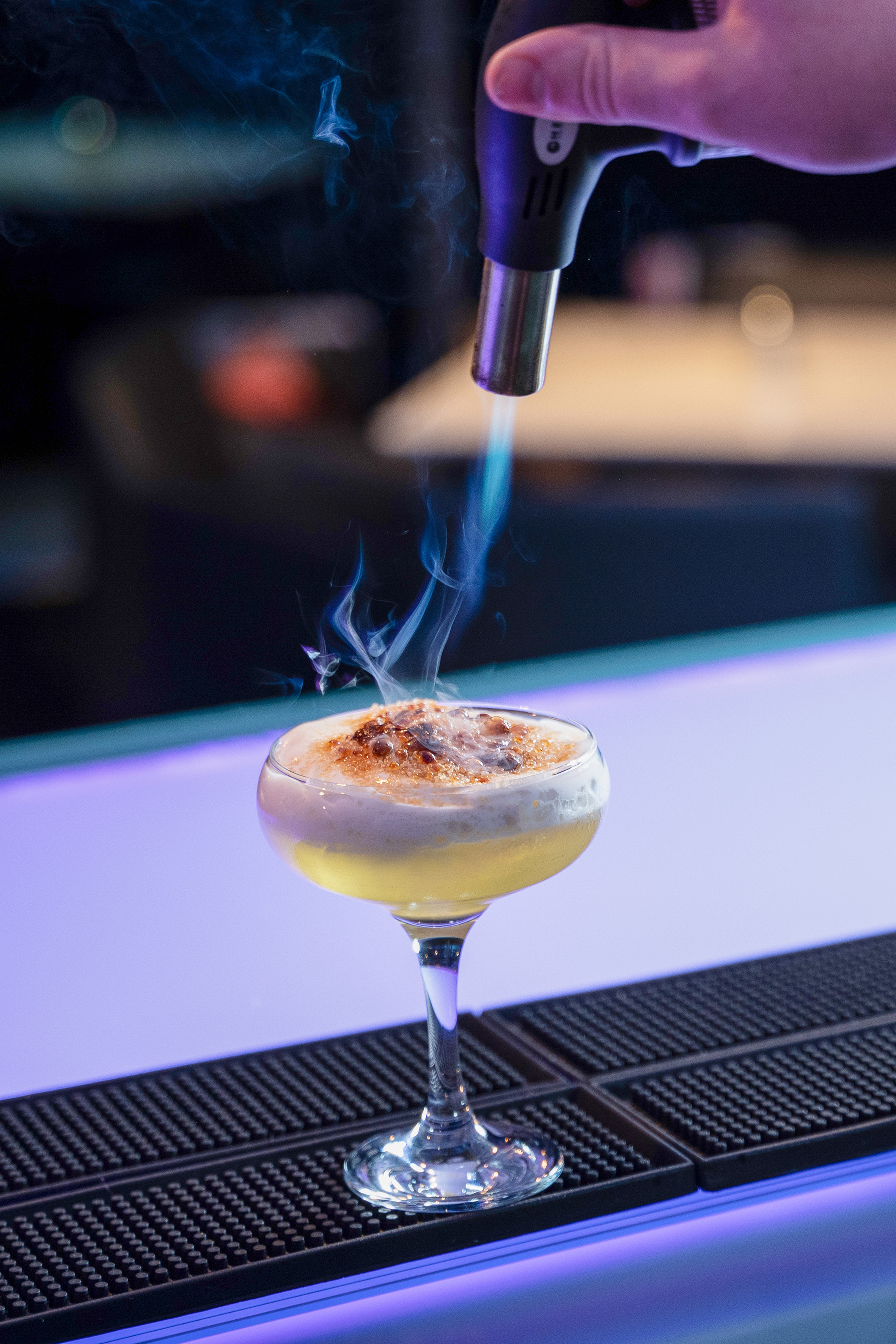 Crème brûlée cocktail being torched by hand, smoke rising from the drink. - Twist Bar, Apéritifs - INNSiDE Dresden, Dresde