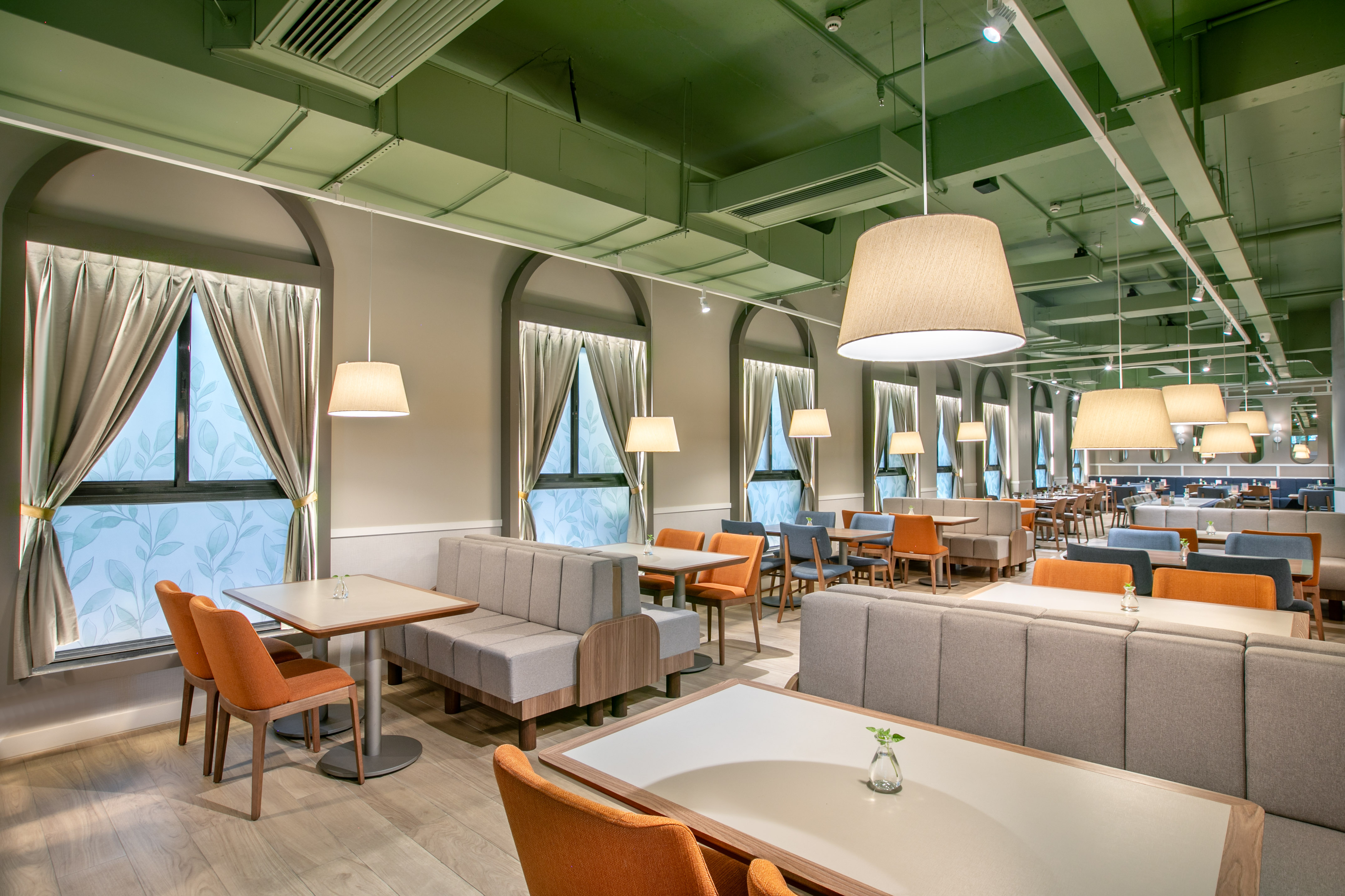 Modern restaurant with booth seating, orange chairs, pendant lights, green ceiling.