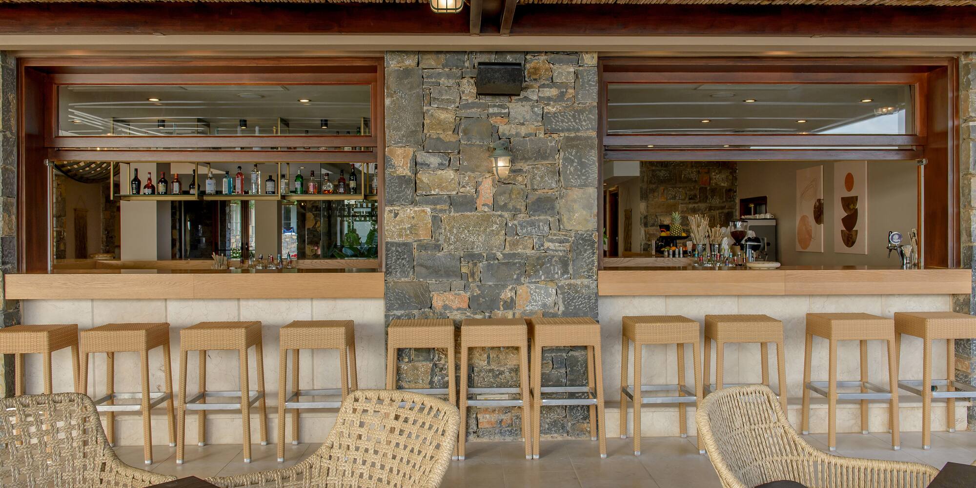 Stylish outdoor resort bar with wicker seating, stone wall, and bamboo ceiling.